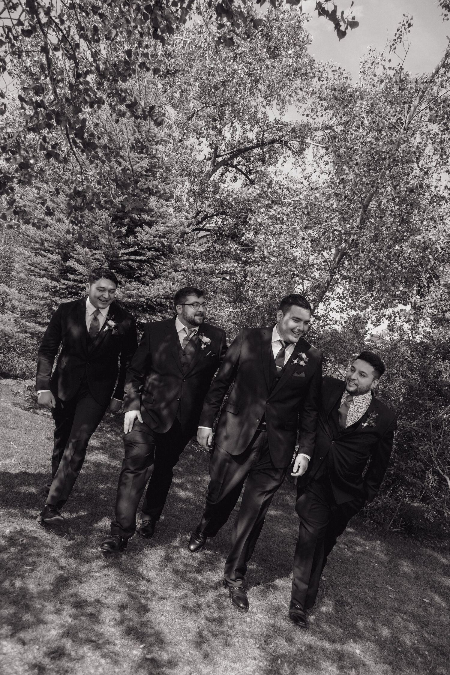 Black and white photo of groom and three groomsmen in dark suits walking together outdoors.