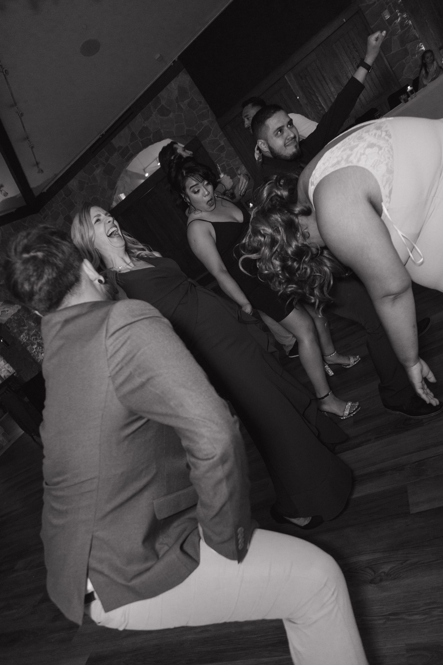 Wedding guests laugh and dance energetically on the dance floor in a black and white photo.