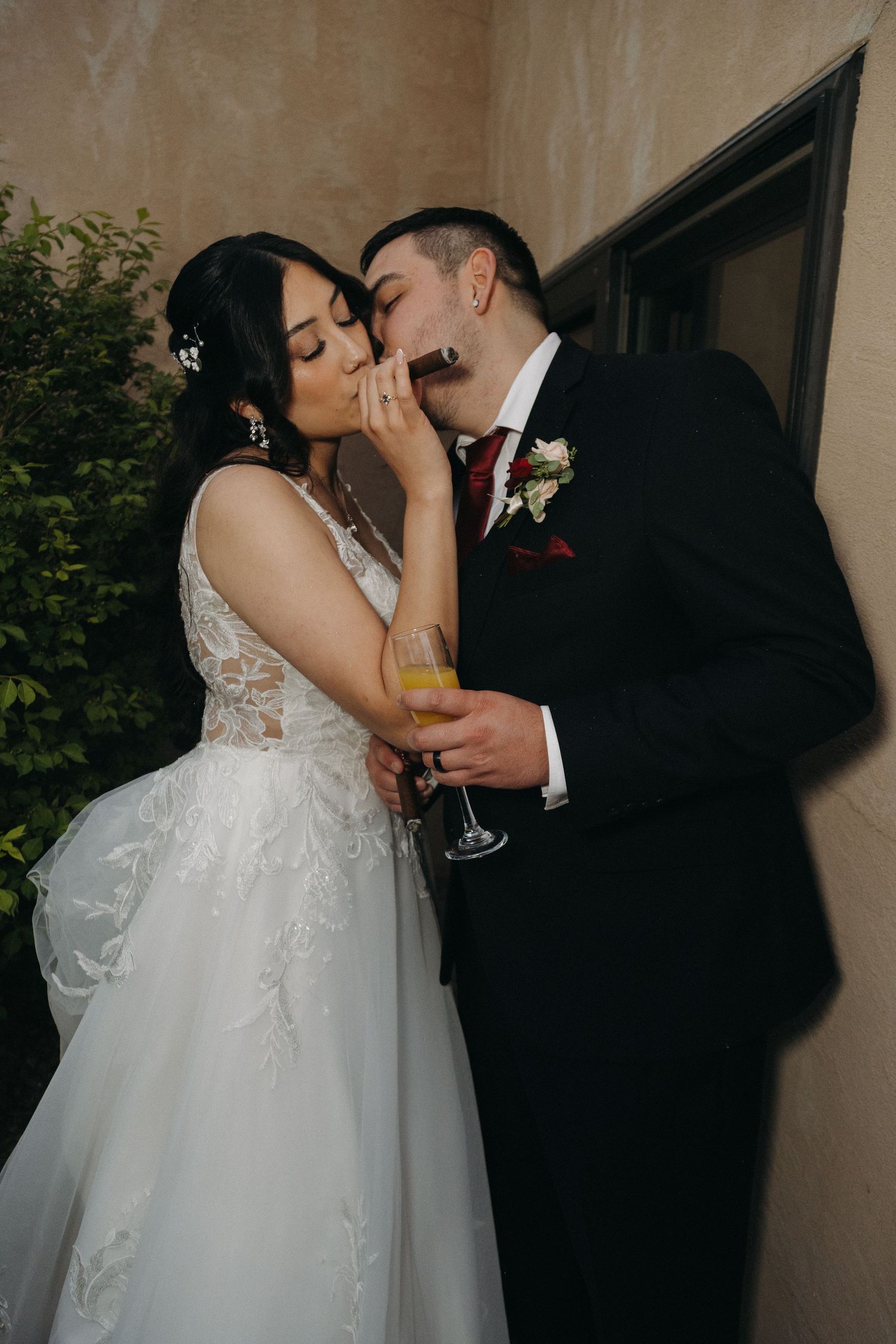 Bride and groom sharing a romantic kiss while holding champagne glasses at their wedding reception.