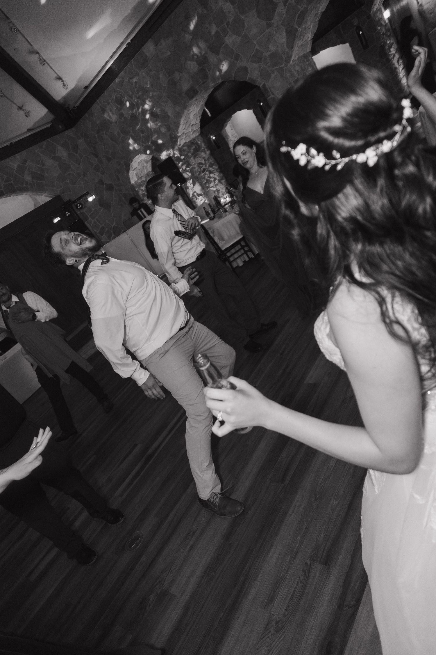 Black and white photo of wedding guests dancing energetically on the dance floor during a lively reception celebration.