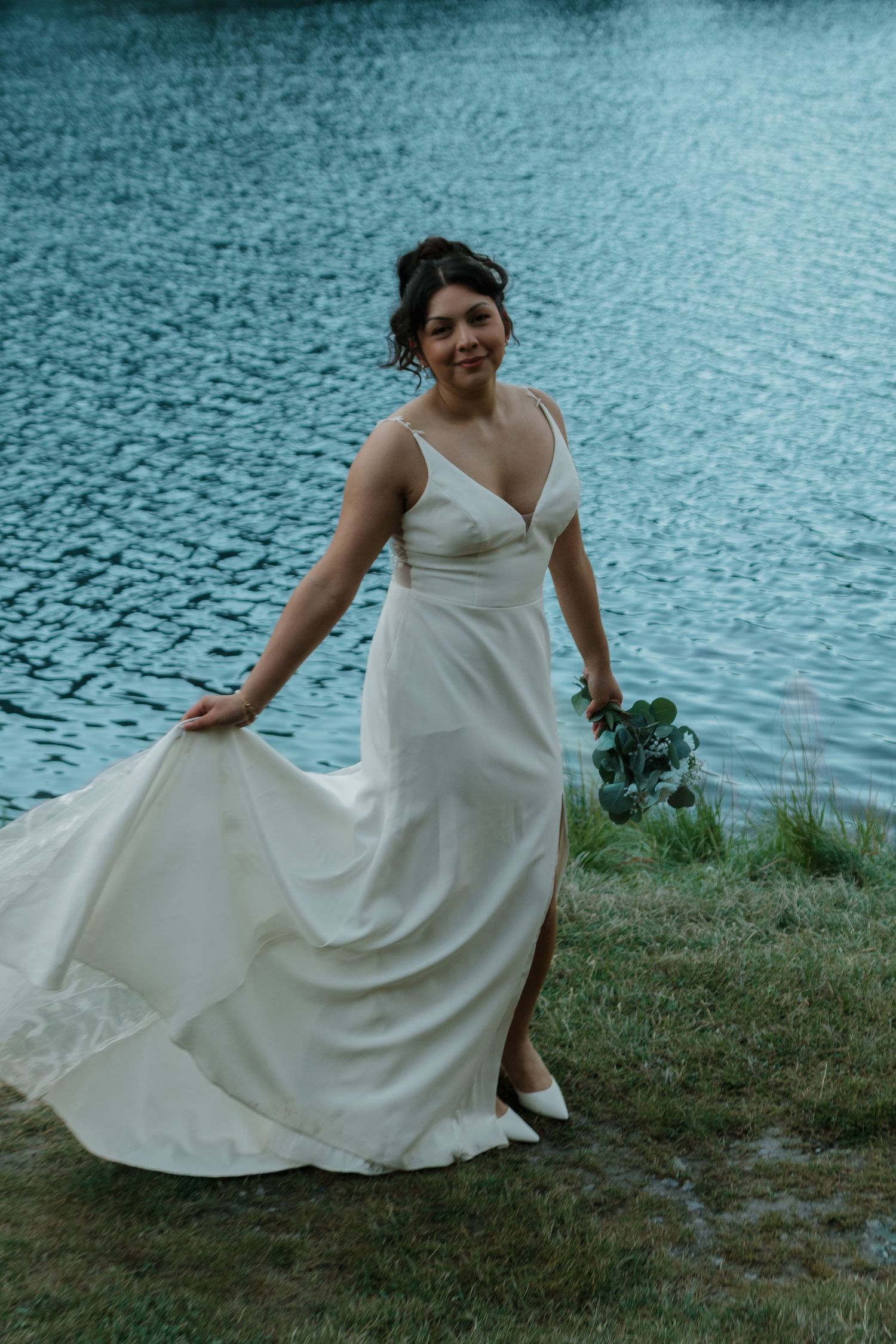 A bride in a flowing white dress twirls by a serene lake.