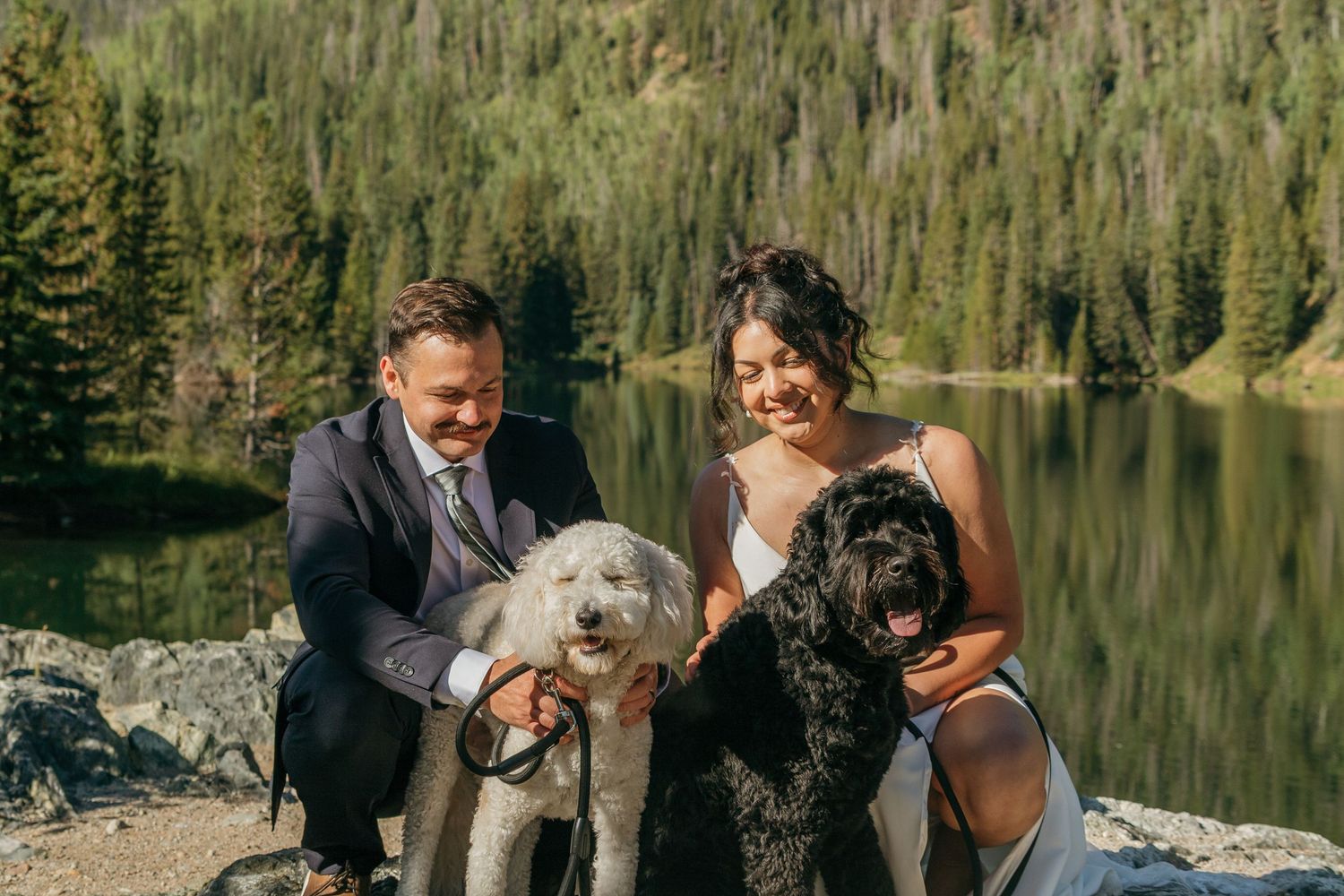 A couple celebrates their wedding day with their dog by a scenic mountain lake.