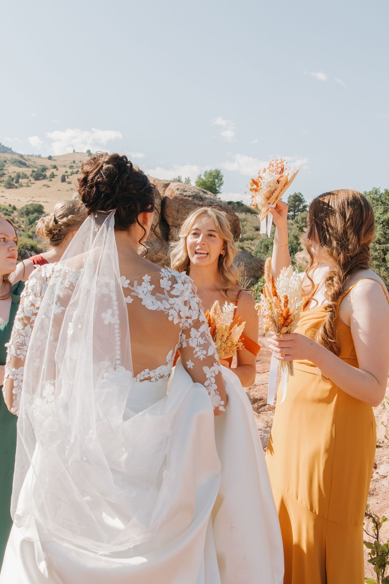 Bridal party in white and yellow dresses celebrating joyfully against mountain backdrop.