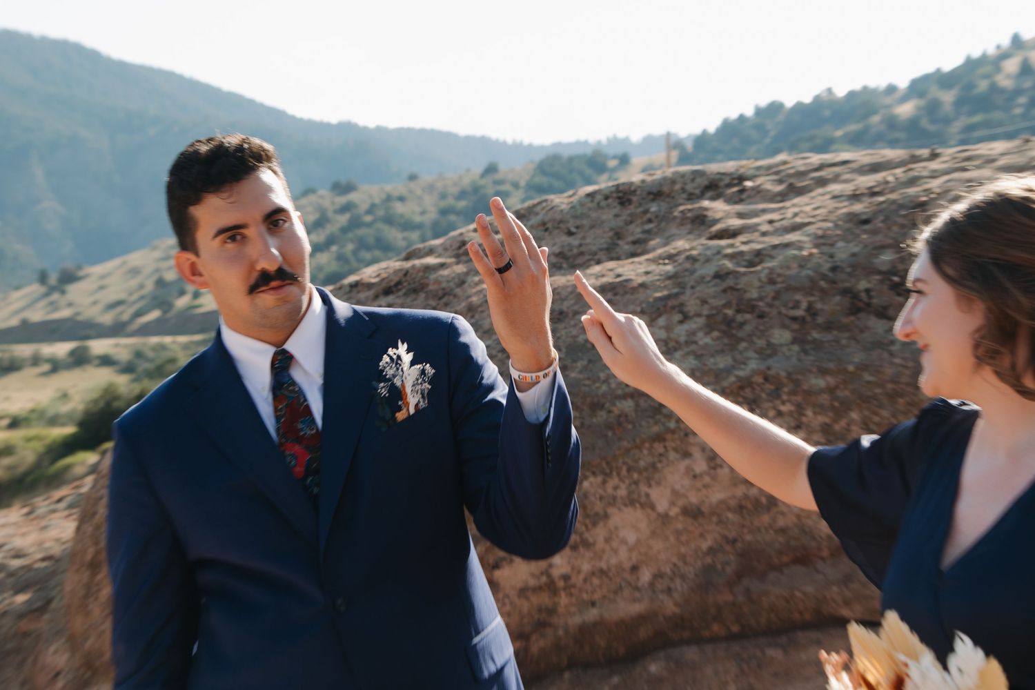Wedding party members interact joyfully with mountain scenery in the background.