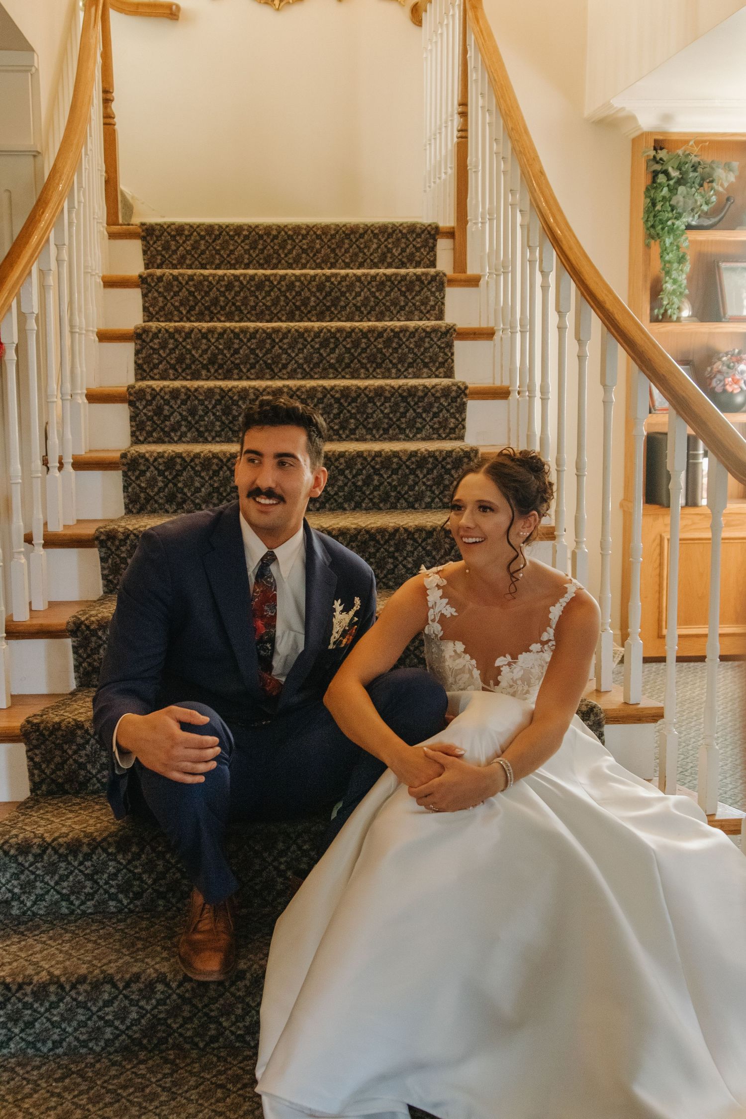 Wedding couple sitting together on carpeted stairs in formal attire.