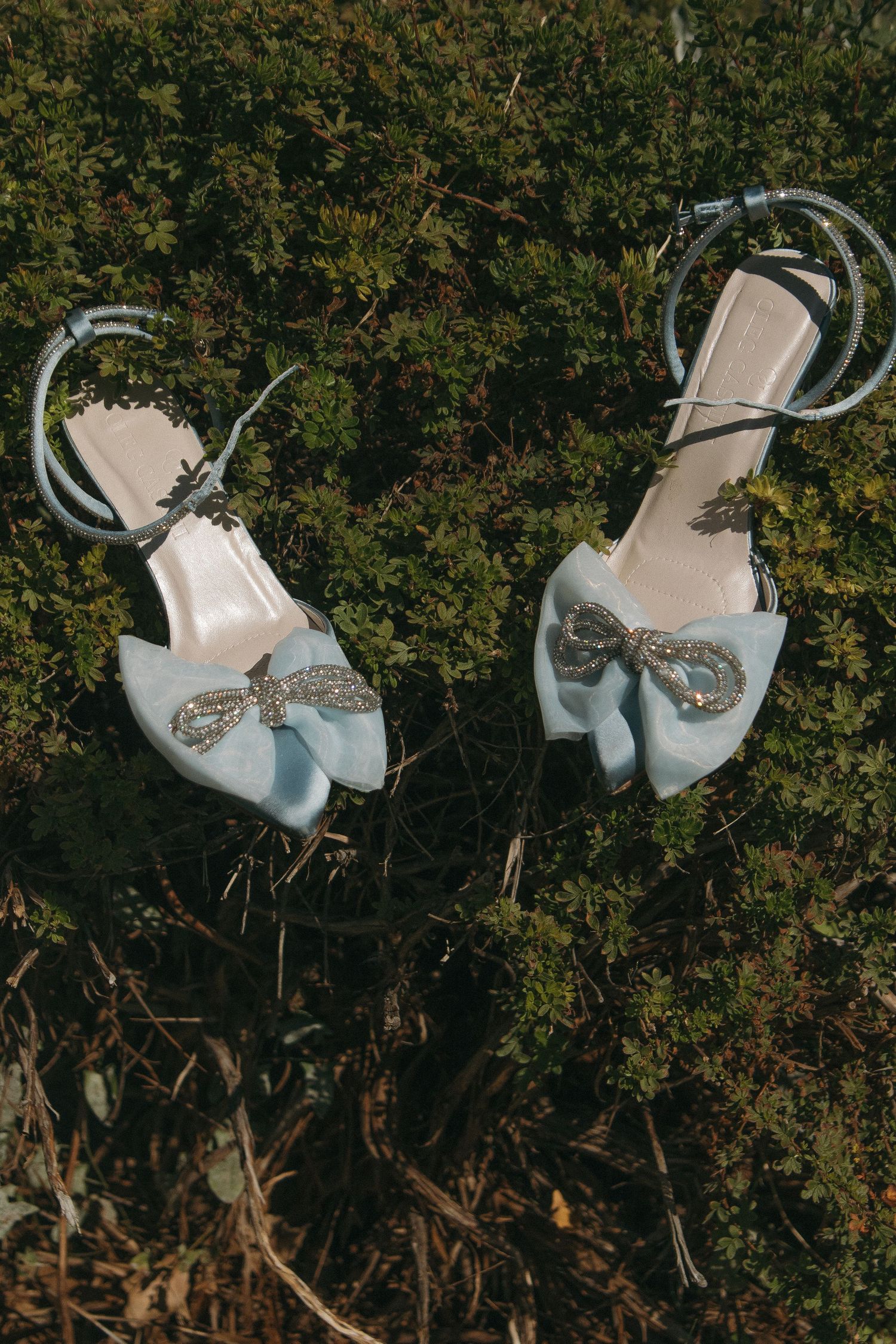 Elegant white bridal shoes with sparkly embellishments displayed against a natural outdoor background.