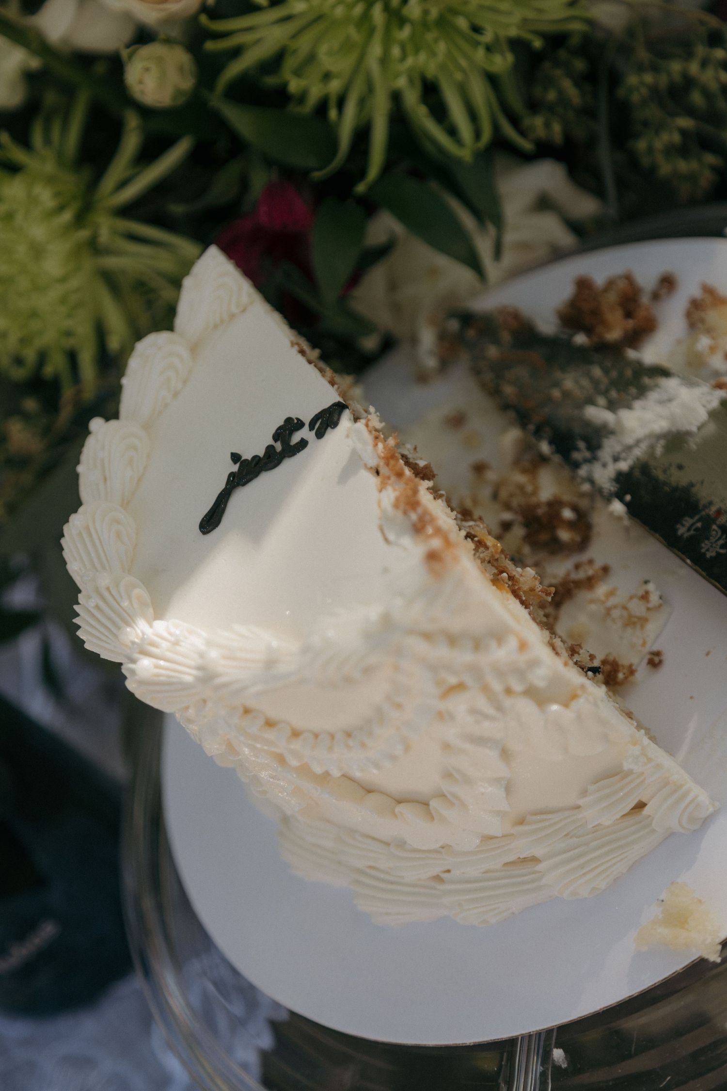 Close-up of sliced white wedding cake with lace detailing and floral arrangement in background.