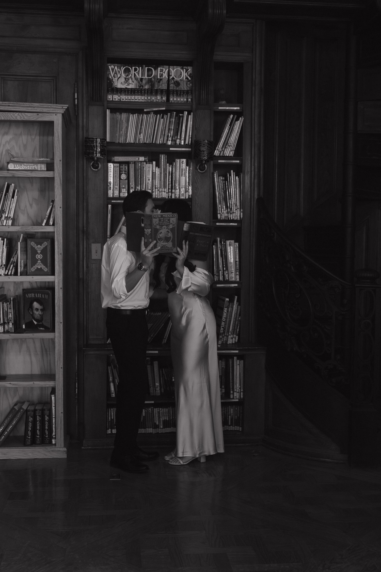 Silhouettes of people moving through a dark library interior with wooden bookshelves.
