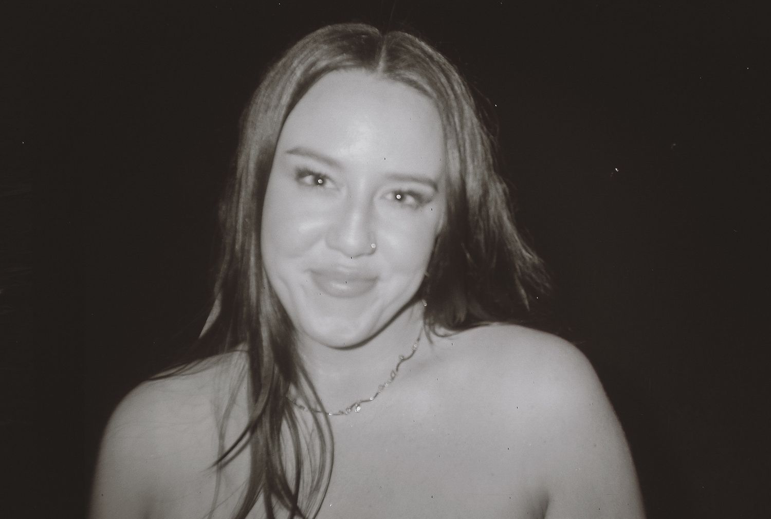 Black and white film portrait of a smiling woman with long hair at a wedding.