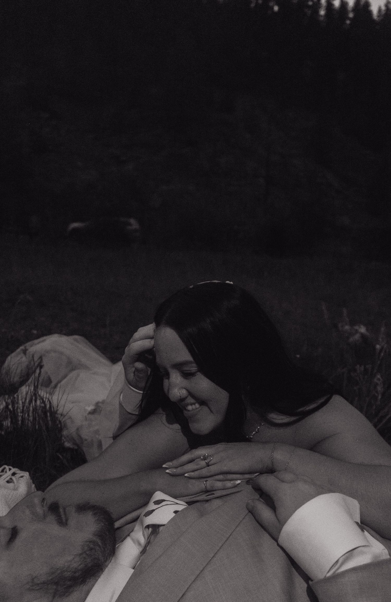 Intimate black and white photo of smiling bride and groom lying together in grass at night.