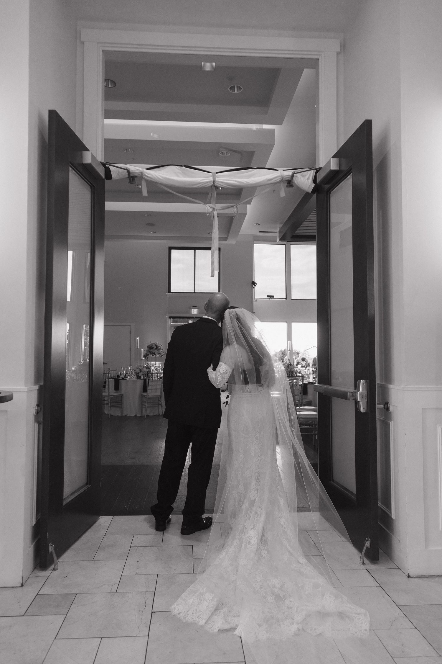 Bride and groom standing at venue entrance doors in elegant black and white wedding photo.