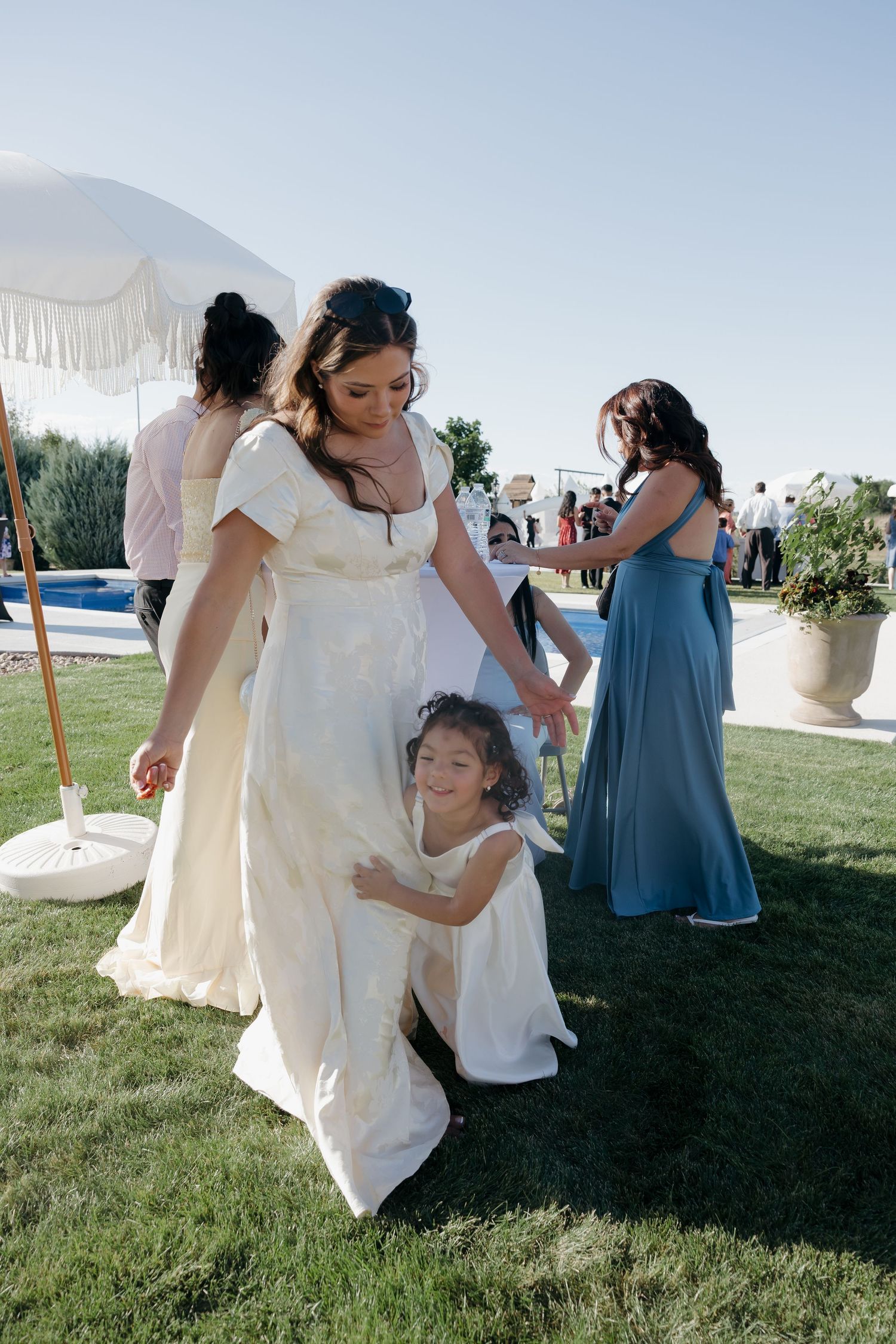 Bride in ivory gown shares sweet moment with young flower girl on wedding reception lawn.