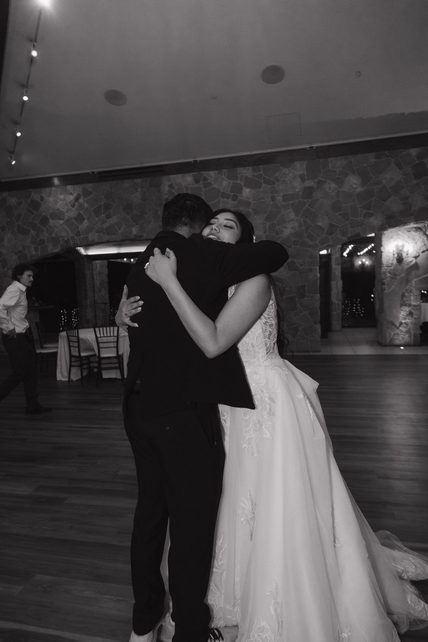 Bride in lace ball gown shares a joyful embrace with groom on the wedding dance floor.