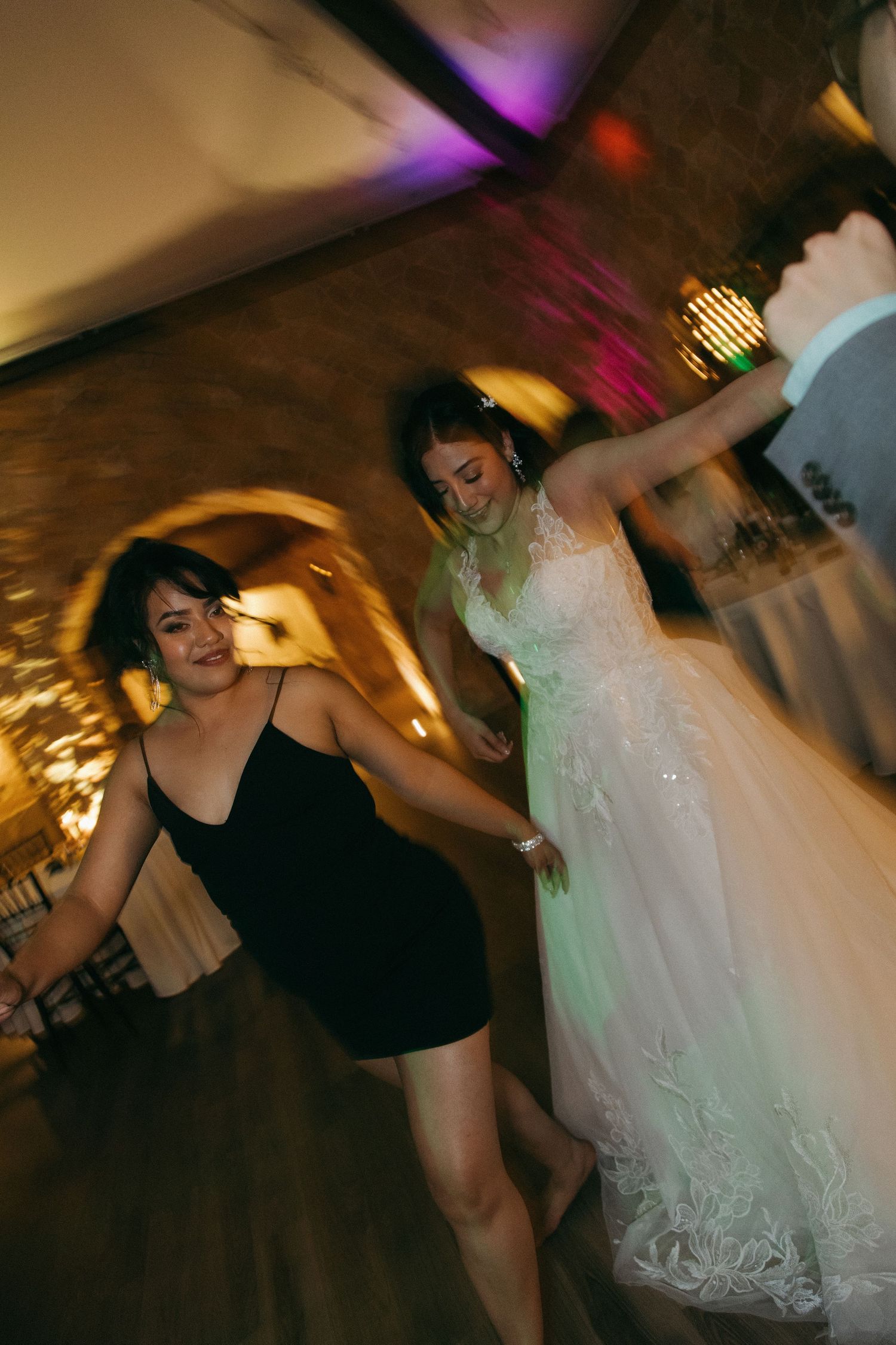 Bride in white gown dancing energetically with a guest in a black dress at the reception.