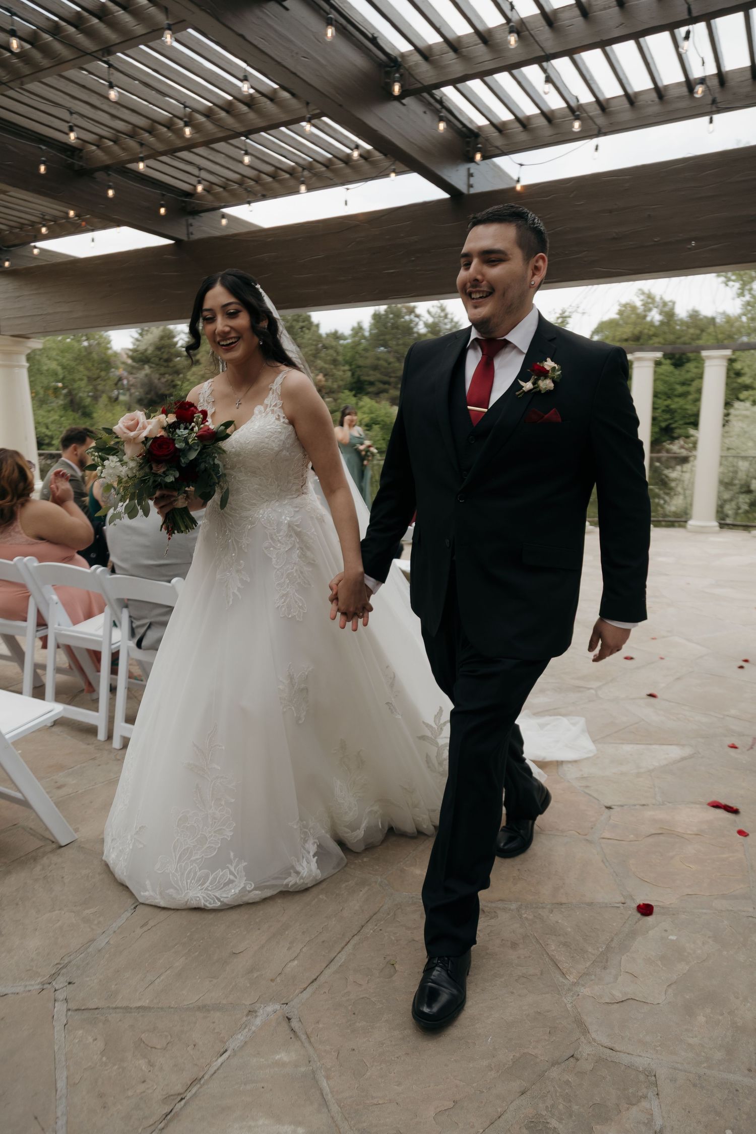 Smiling bride and groom hold hands walking back down the aisle after outdoor wedding ceremony.
