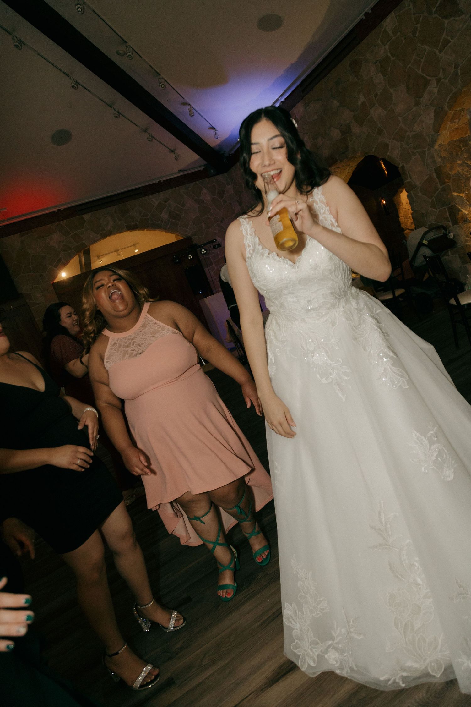 Bride in white lace gown dancing and drinking at wedding reception celebration.