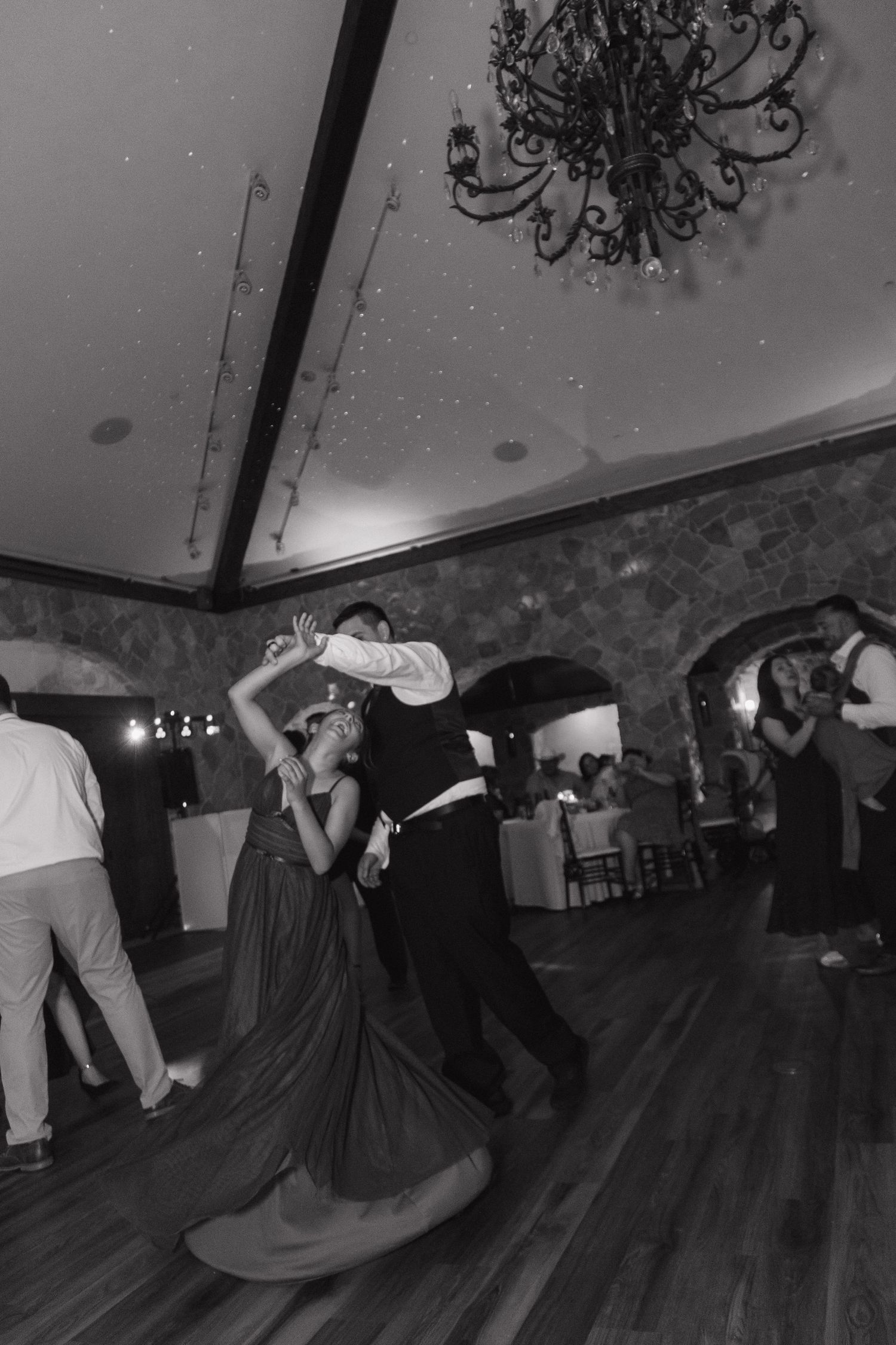 Black and white photo of couple dancing dramatically under chandelier at wedding reception.