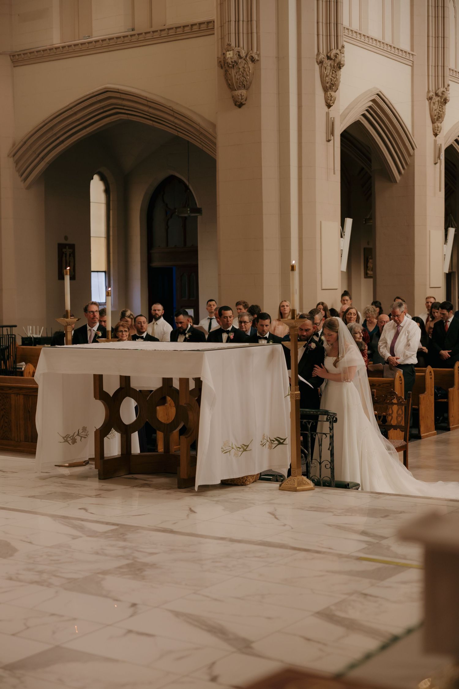 Bride and groom kneeling at altar during Catholic wedding ceremony in elegant church.