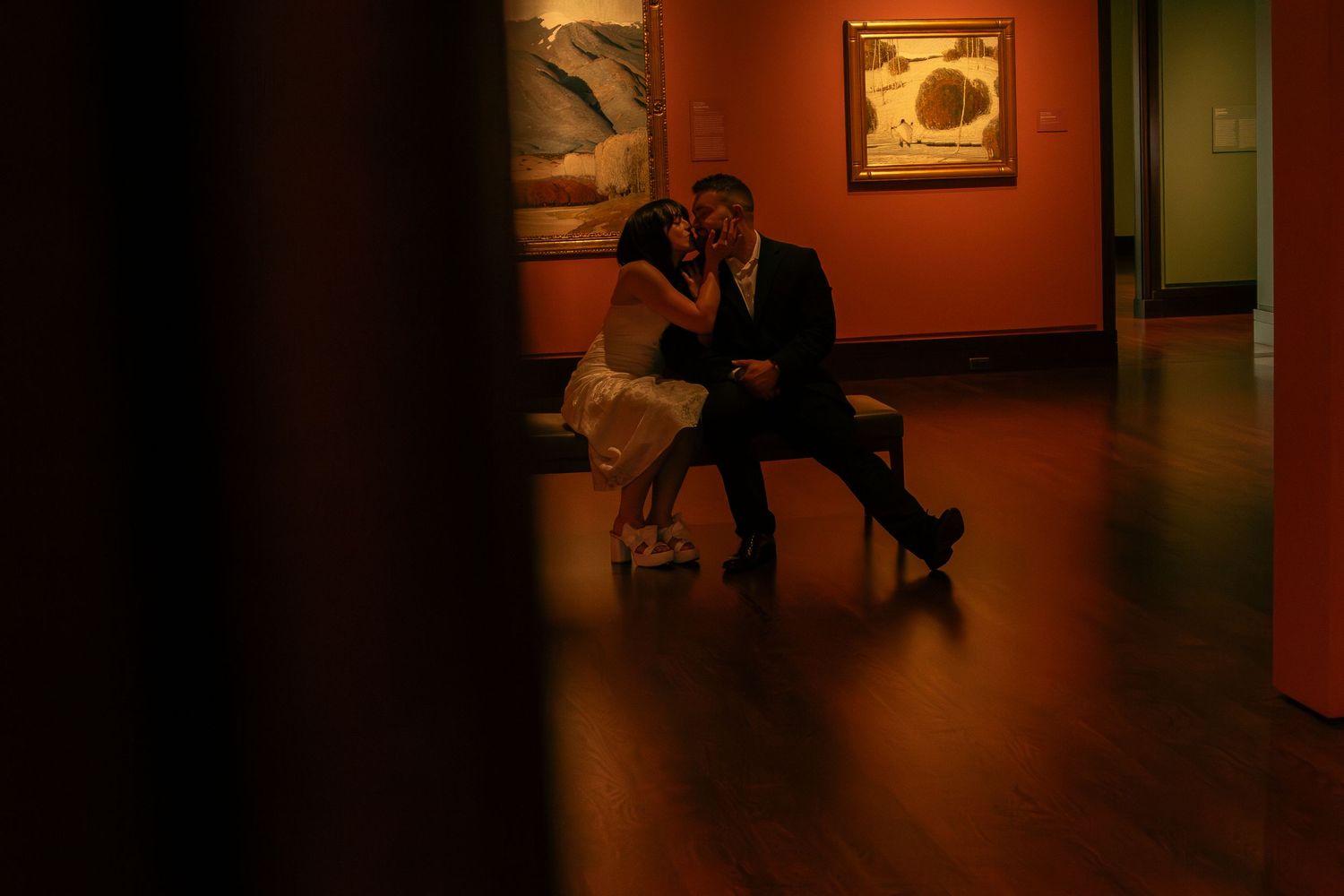 Couple dancing in dimly lit museum gallery space with artwork on walls.