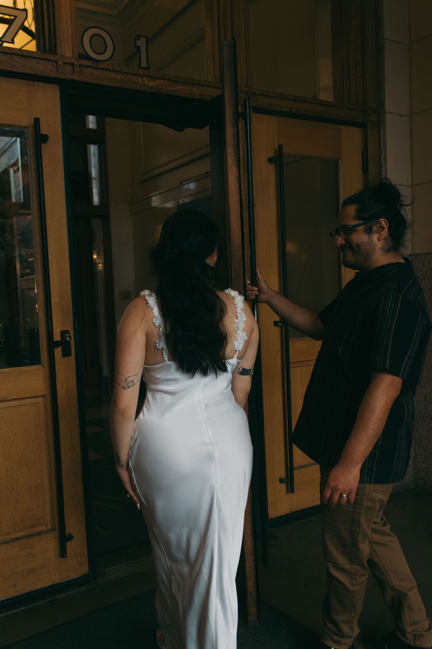 A couple shares an intimate moment by glass doors in an elegant hallway setting.
