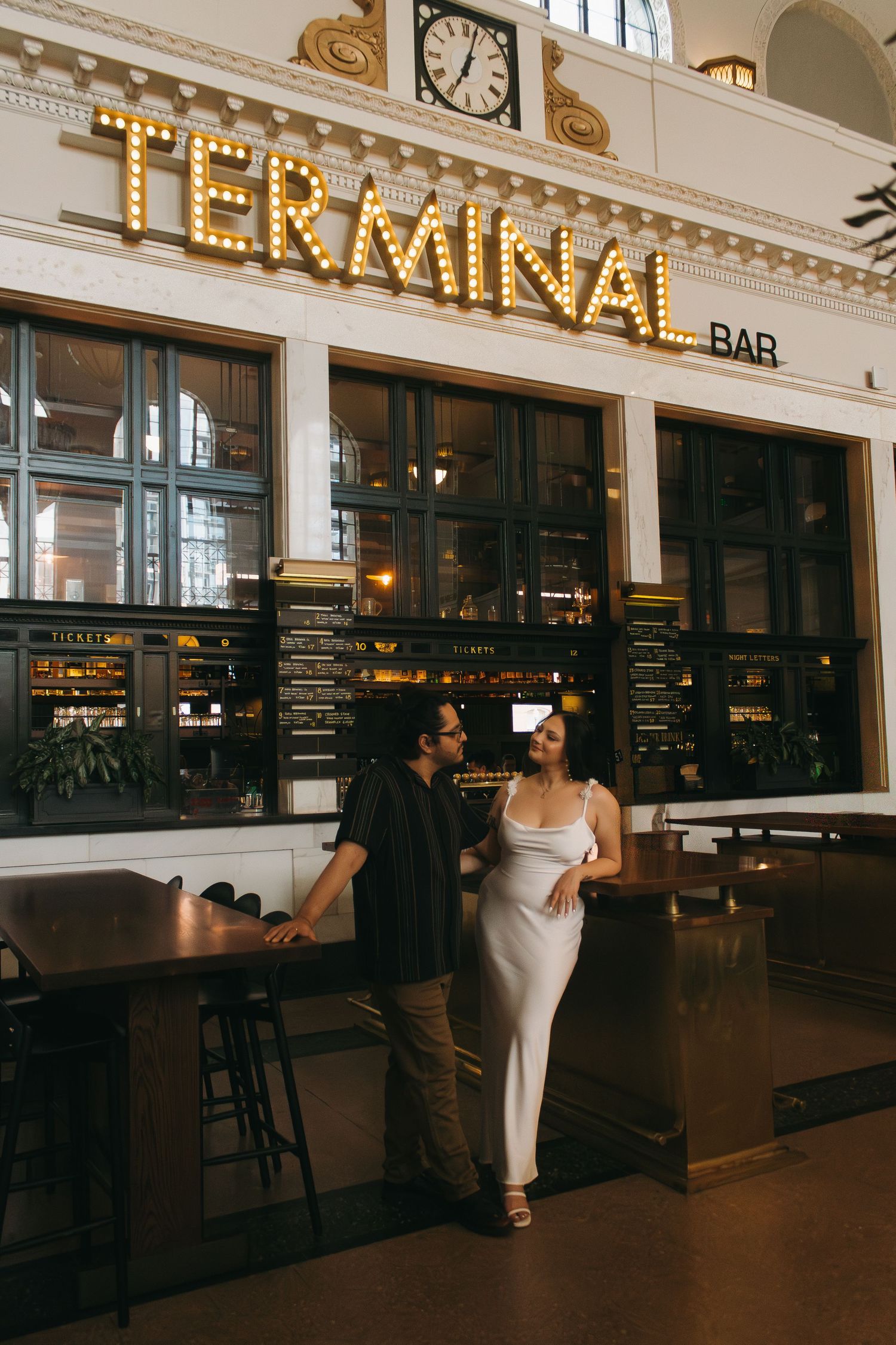 A couple poses together inside Terminal Bar with illuminated signage and vintage decor.