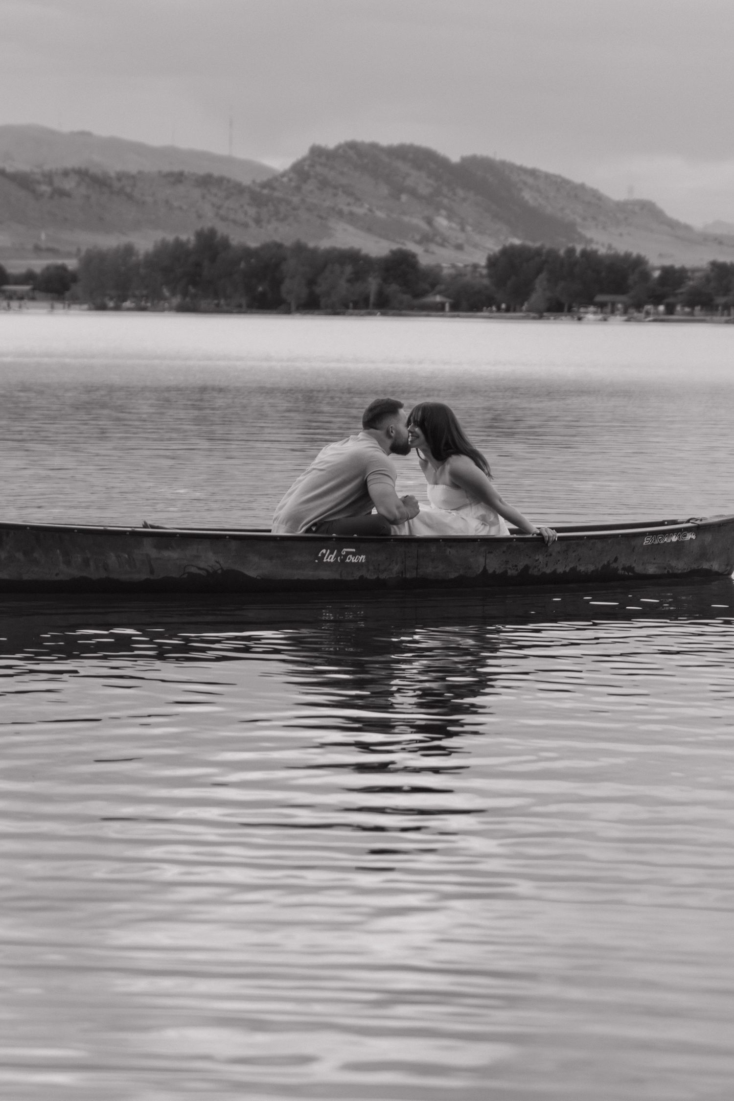 A couple embraces while sitting in a canoe against a mountainous black and white landscape.