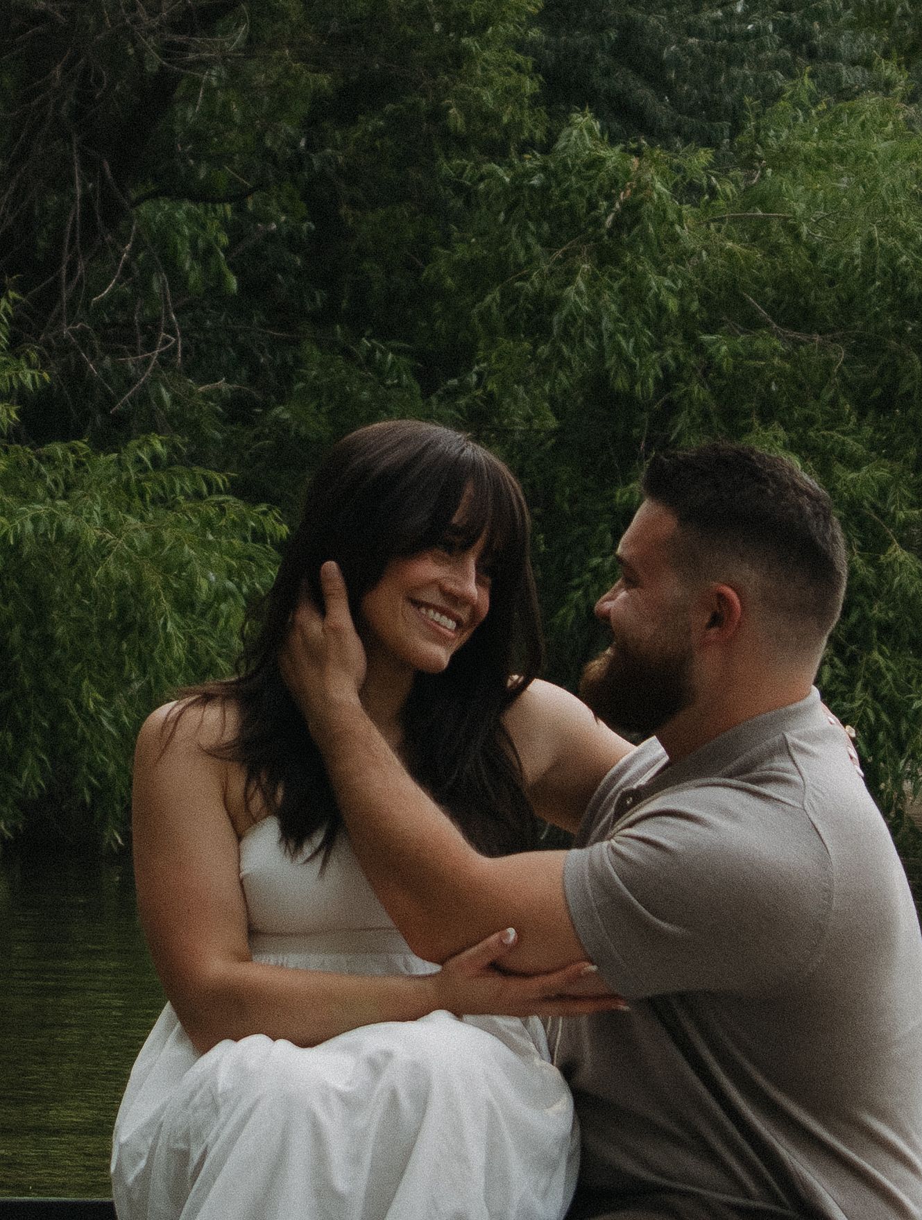 A romantic couple embraces by a tranquil lake surrounded by lush green trees during an intimate photo session.