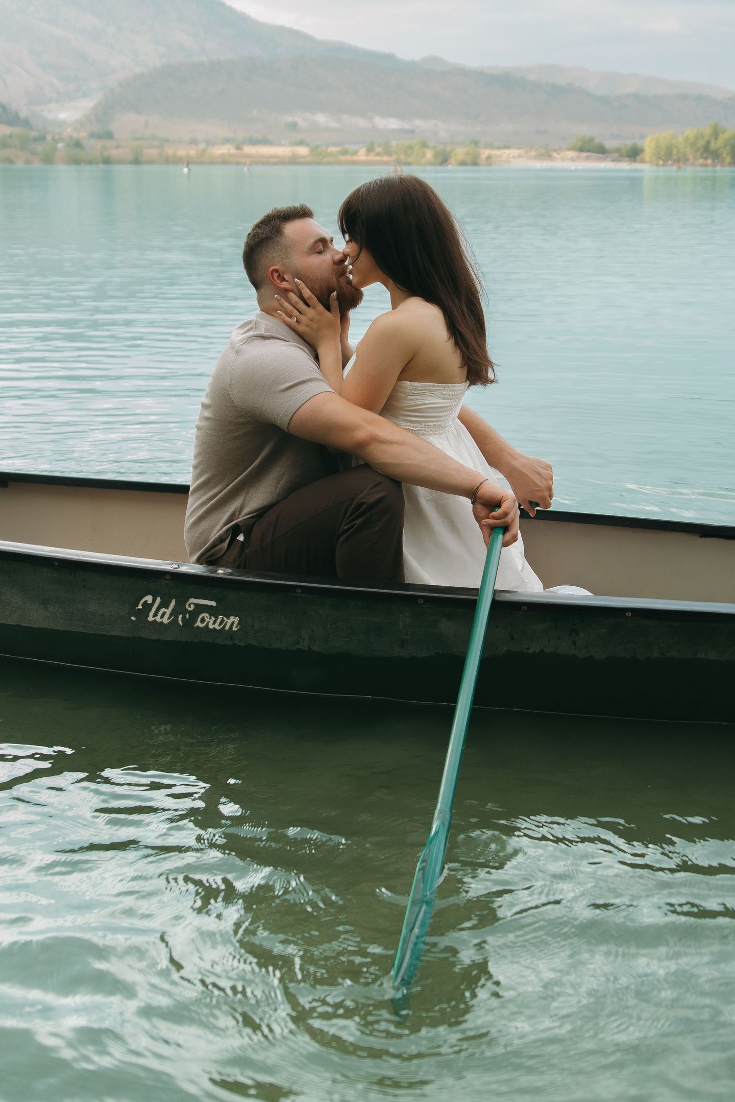 A couple shares a romantic moment in a boat on a turquoise mountain lake.