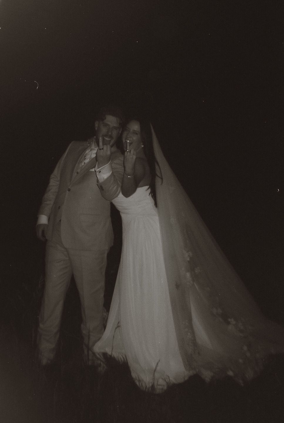 Vintage-style black and white photo of bride and groom posing together at night after wedding ceremony.