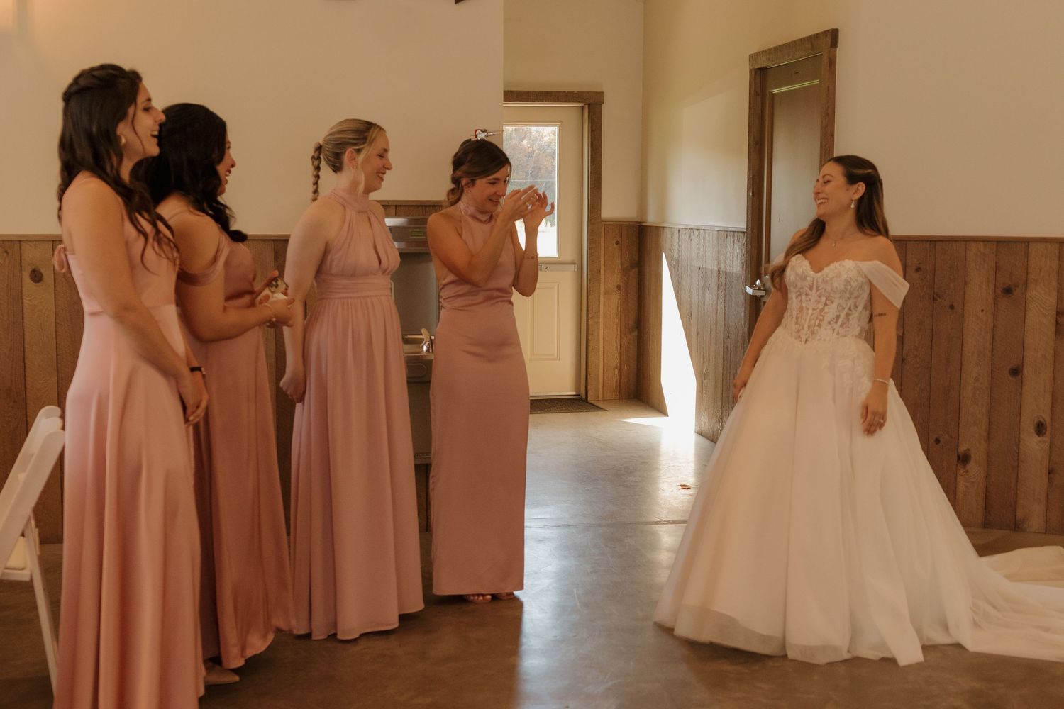 Wedding party members in pink bridesmaid dresses and white gown getting ready in a rustic venue.