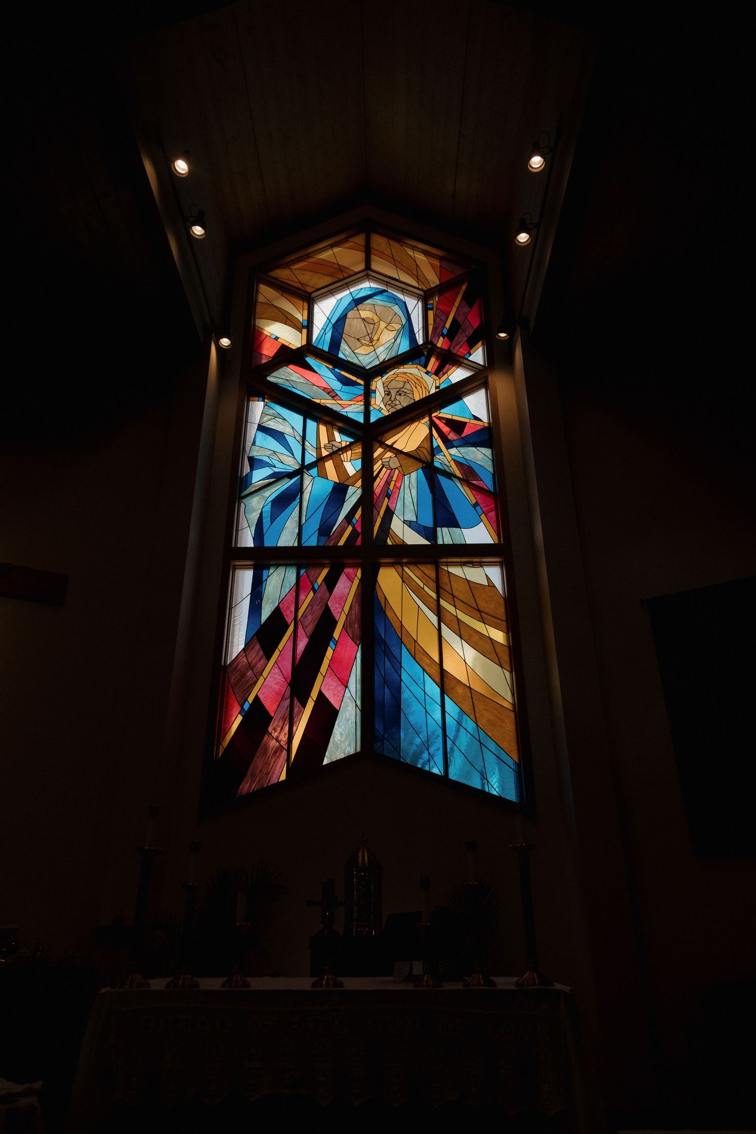 A stunning tall stained glass window illuminates a dark church interior with colorful light.