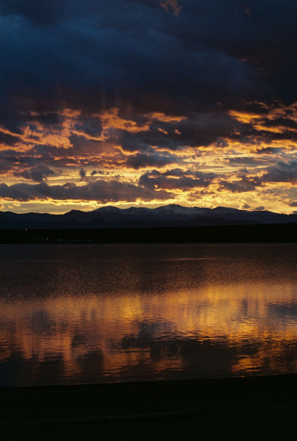 Dramatic sunset over a lake with dark clouds and golden reflections on the water's surface.
