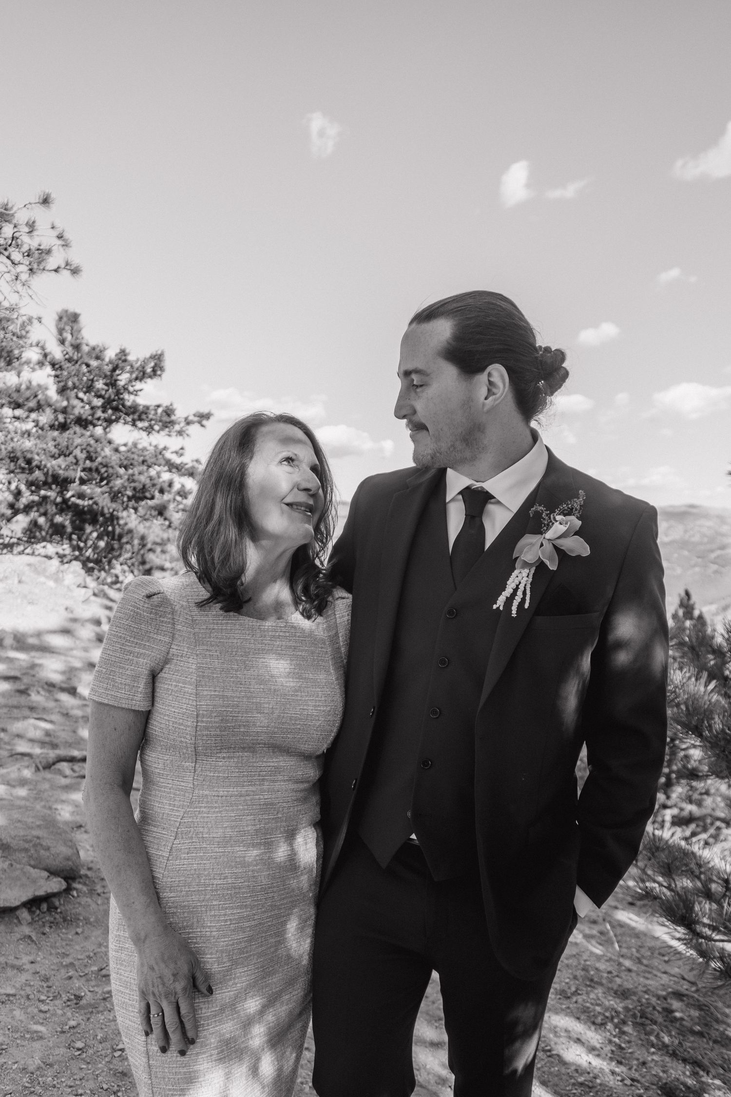 Black and white portrait of a groom in a dark suit with boutonniere standing beside a woman outdoors.