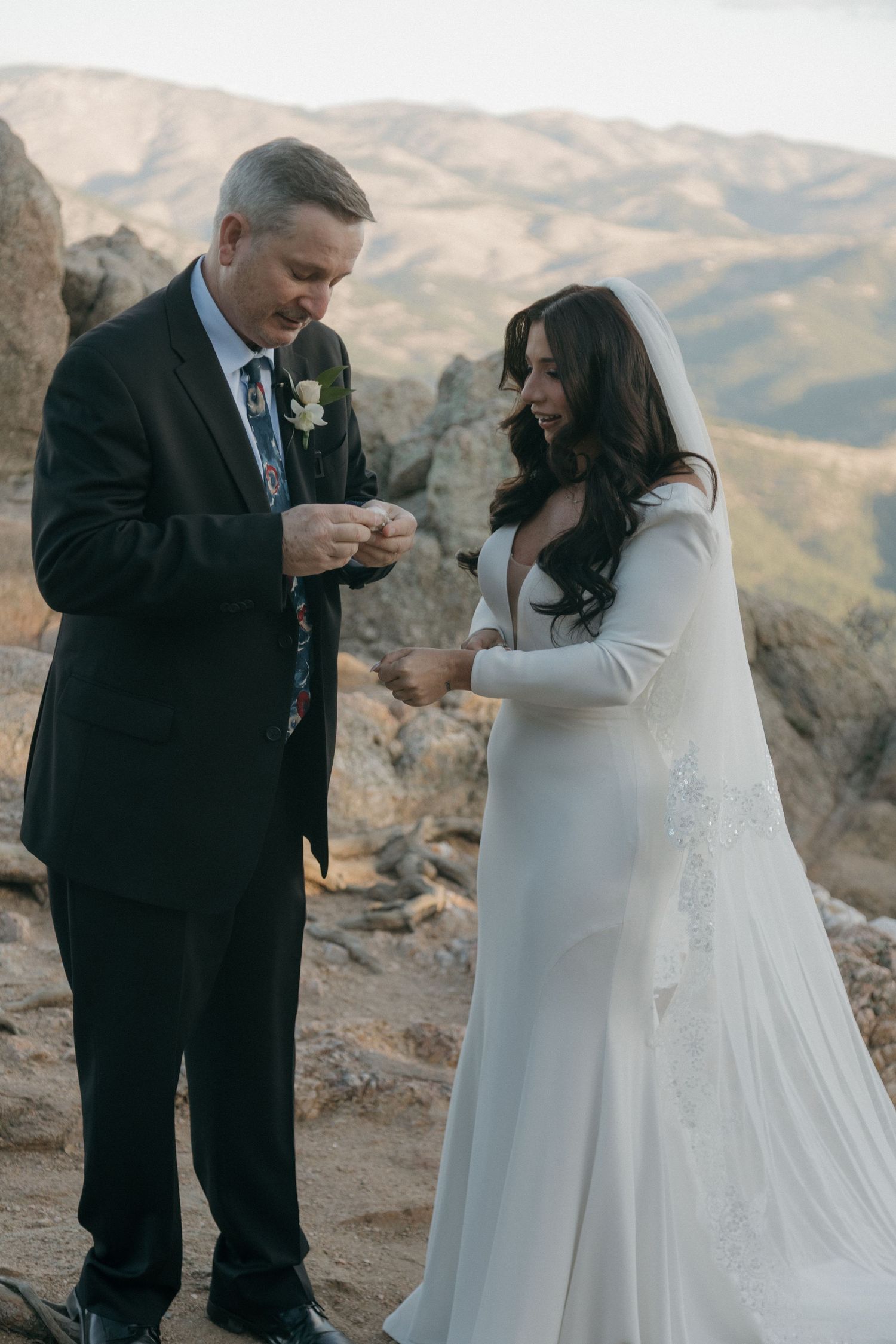 Groom placing wedding ring on brides finger during outdoor mountain elopement ceremony at sunset.