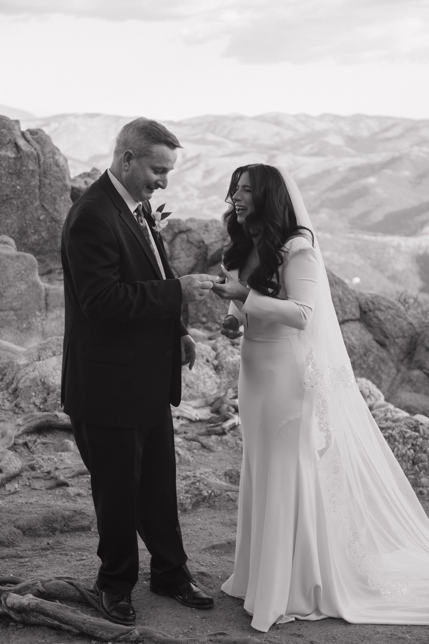 Bride and groom exchange rings on a rocky mountain overlook in black and white wedding photo.