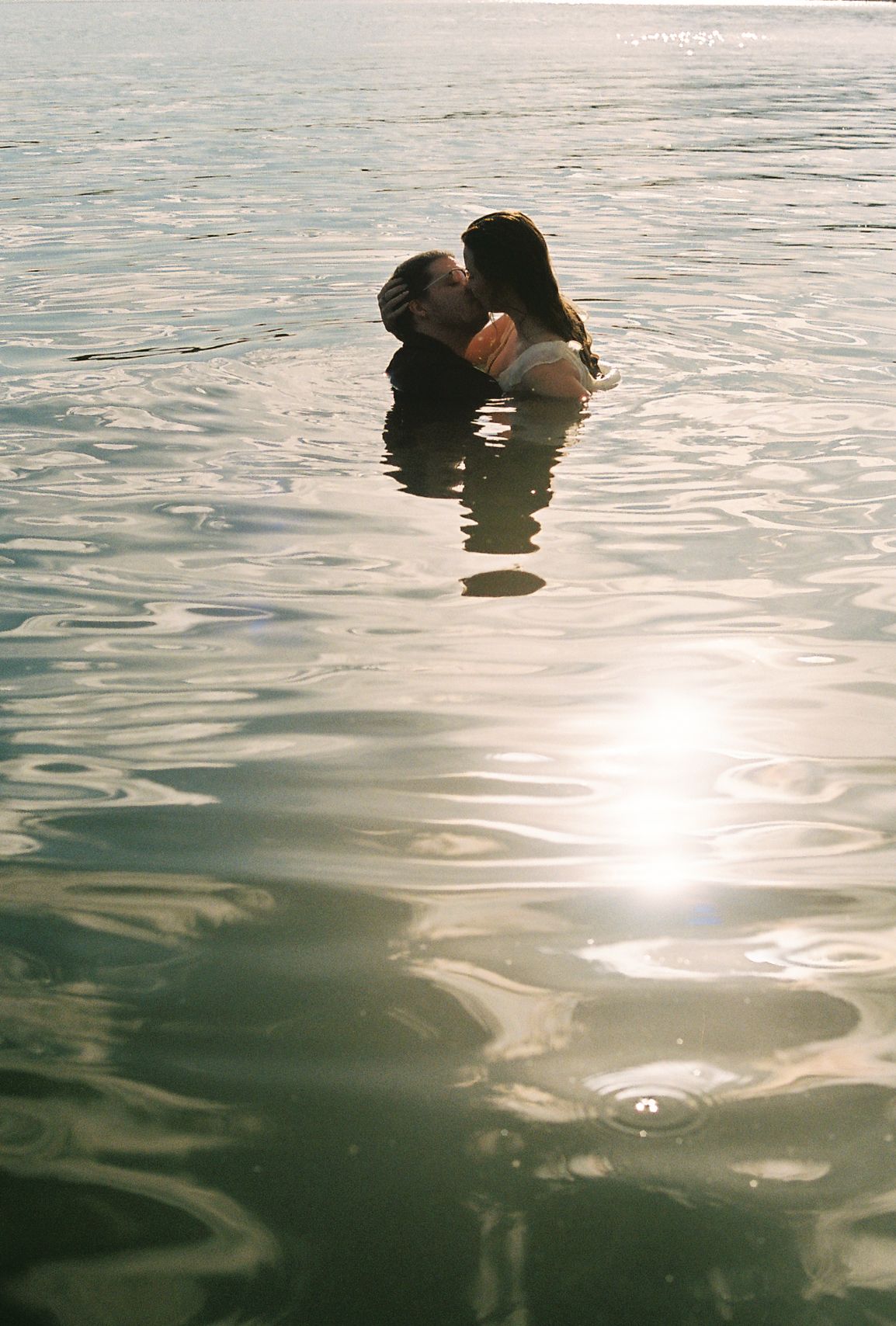 Romantic couple kissing in a sunlit lake with golden light reflecting on the water surface.
