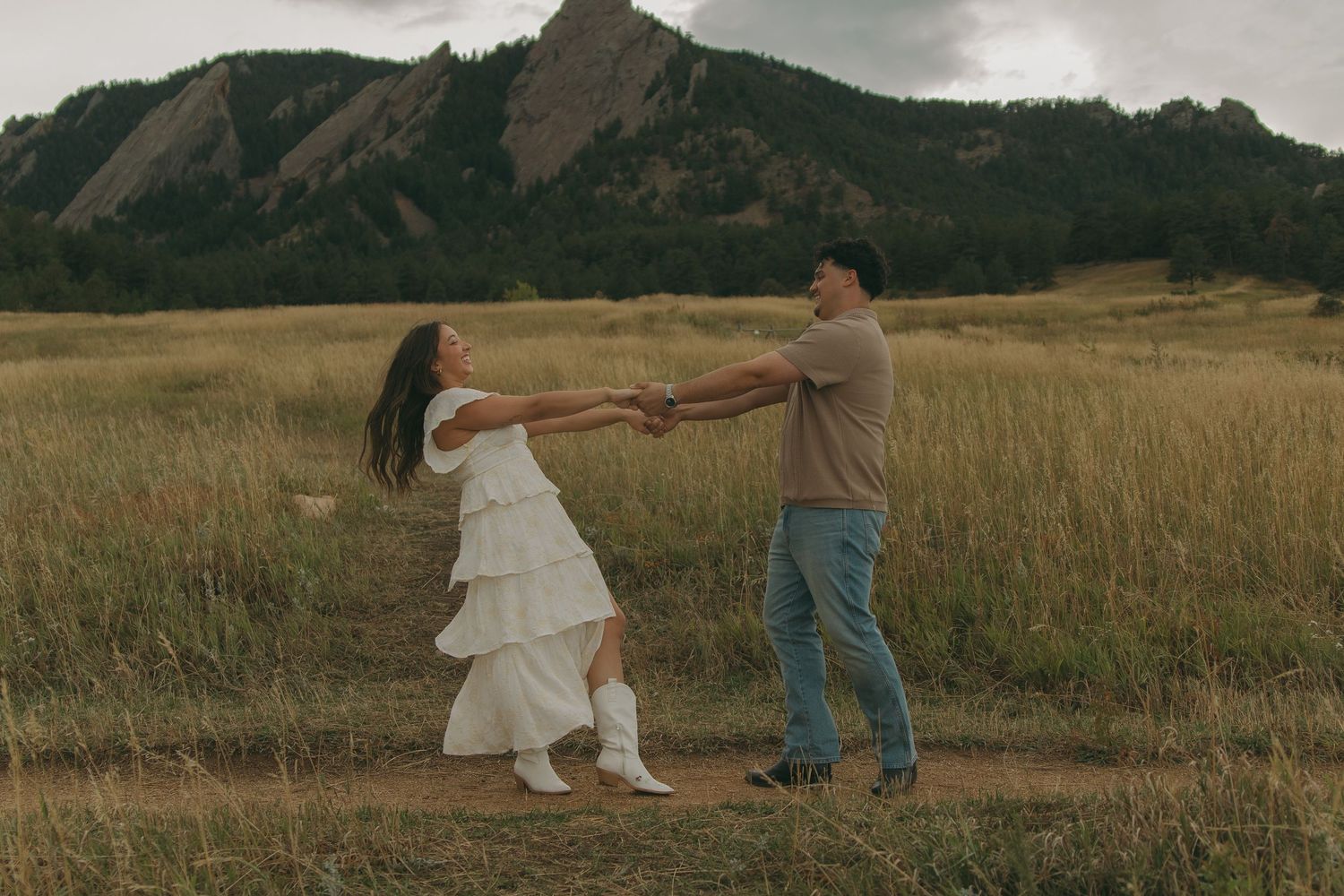 Couple dancing and spinning joyfully in a field with the stunning Flatirons rock formations in background.
