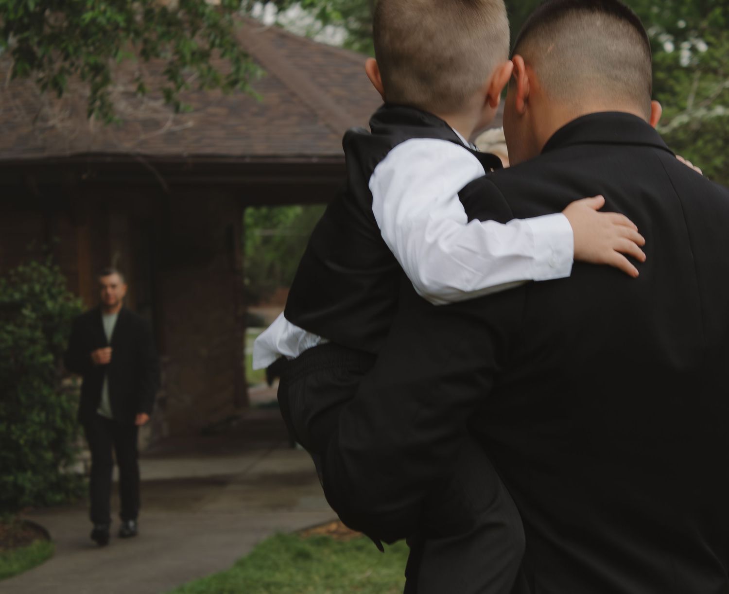 Group in formal attire stands together outdoors during wedding event.