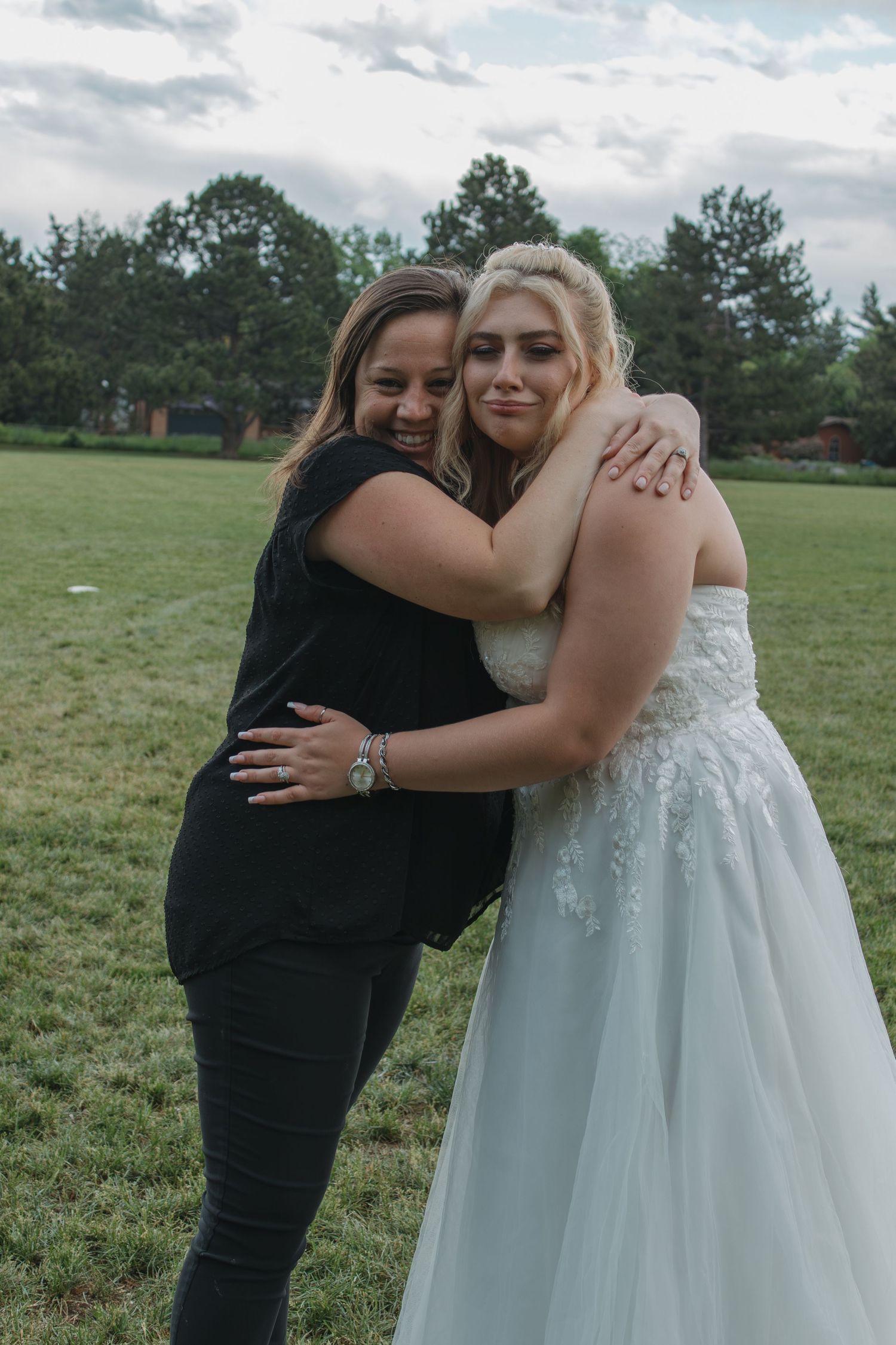 Emotional embrace between two people at outdoor wedding, one in white dress and one in black.