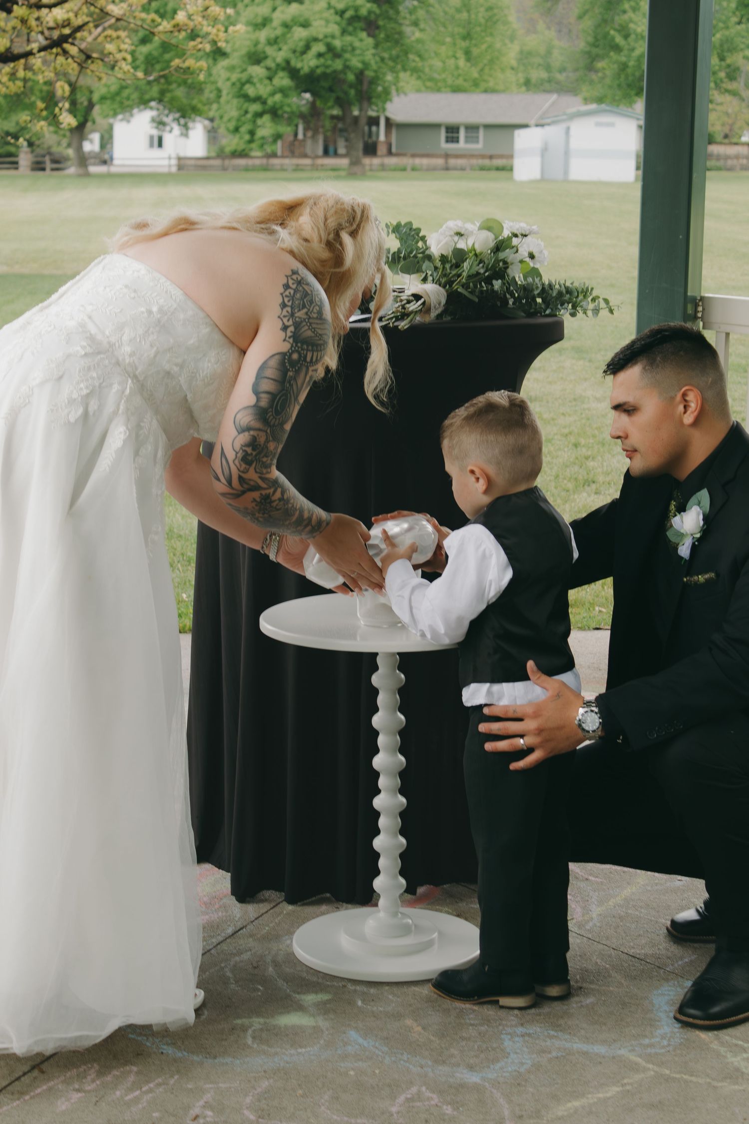 Wedding ceremony participants gather around a decorative white pedestal during the service.