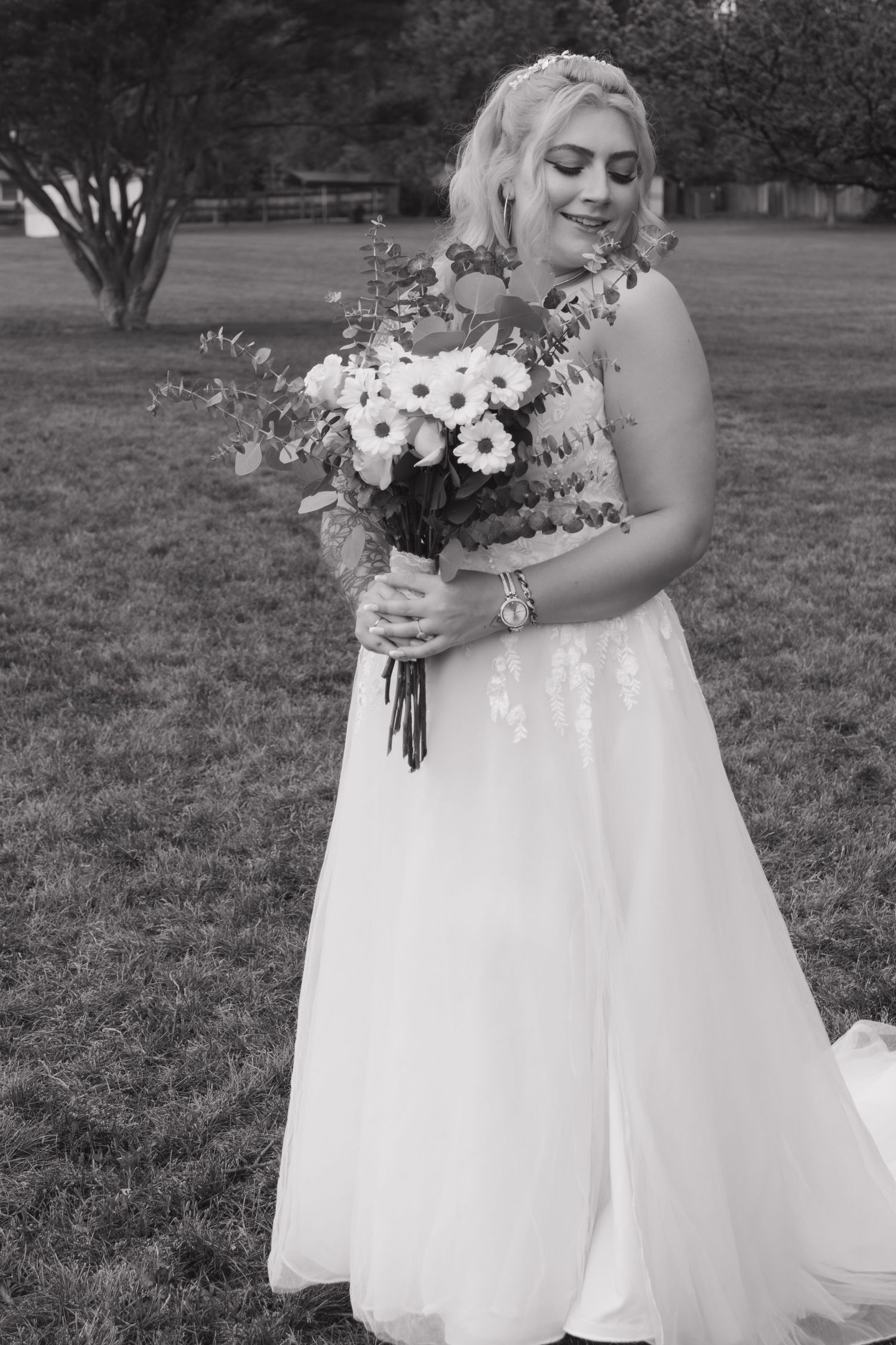 A black and white photo showcasing a wedding dress and floral bouquet in an outdoor setting.