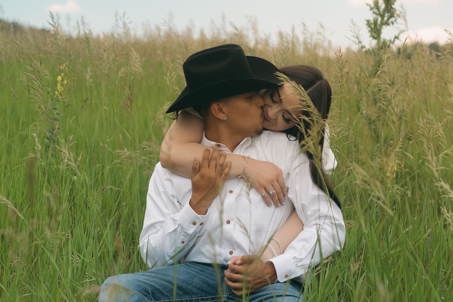 Couple in white shirts and cowboy hat embracing in a sunlit meadow.