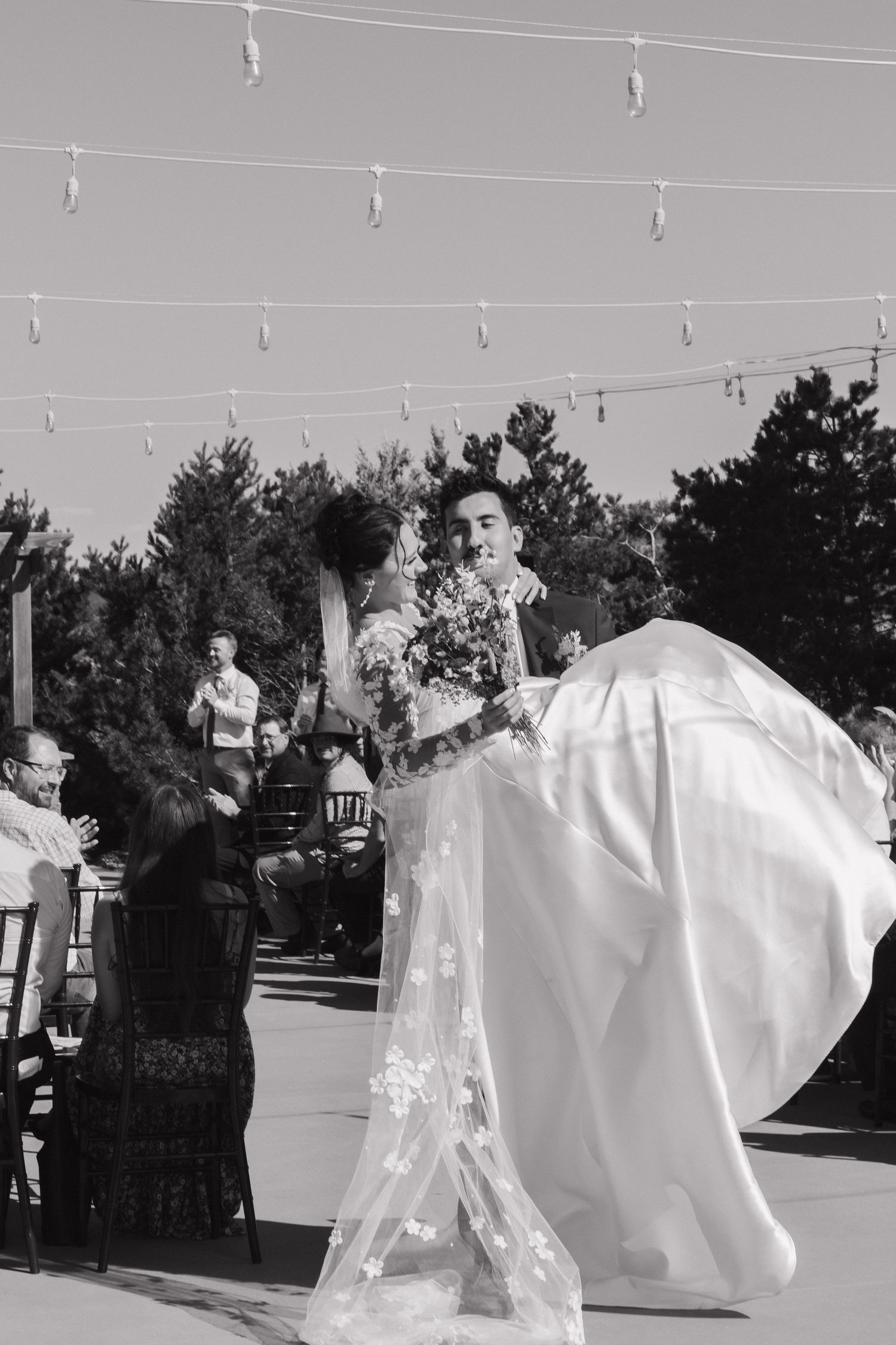 Black and white photo showing billowing wedding dress train against outdoor backdrop.
