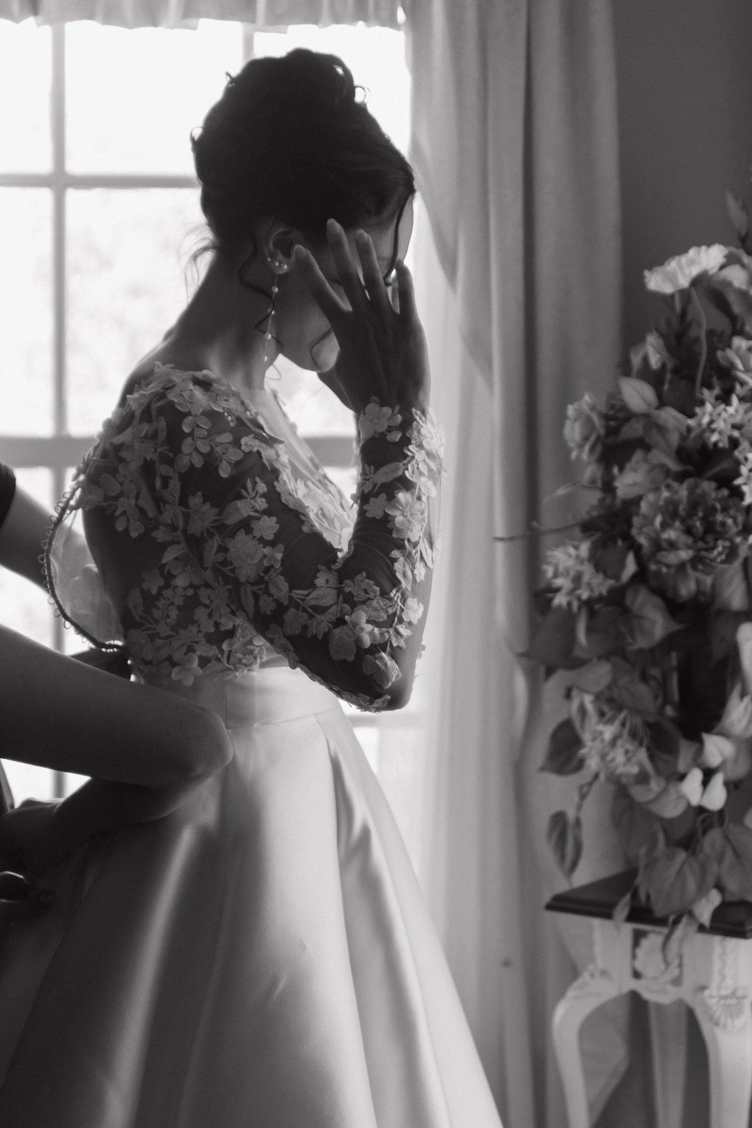 Black and white photo of a bride's dress with floral details by a window.