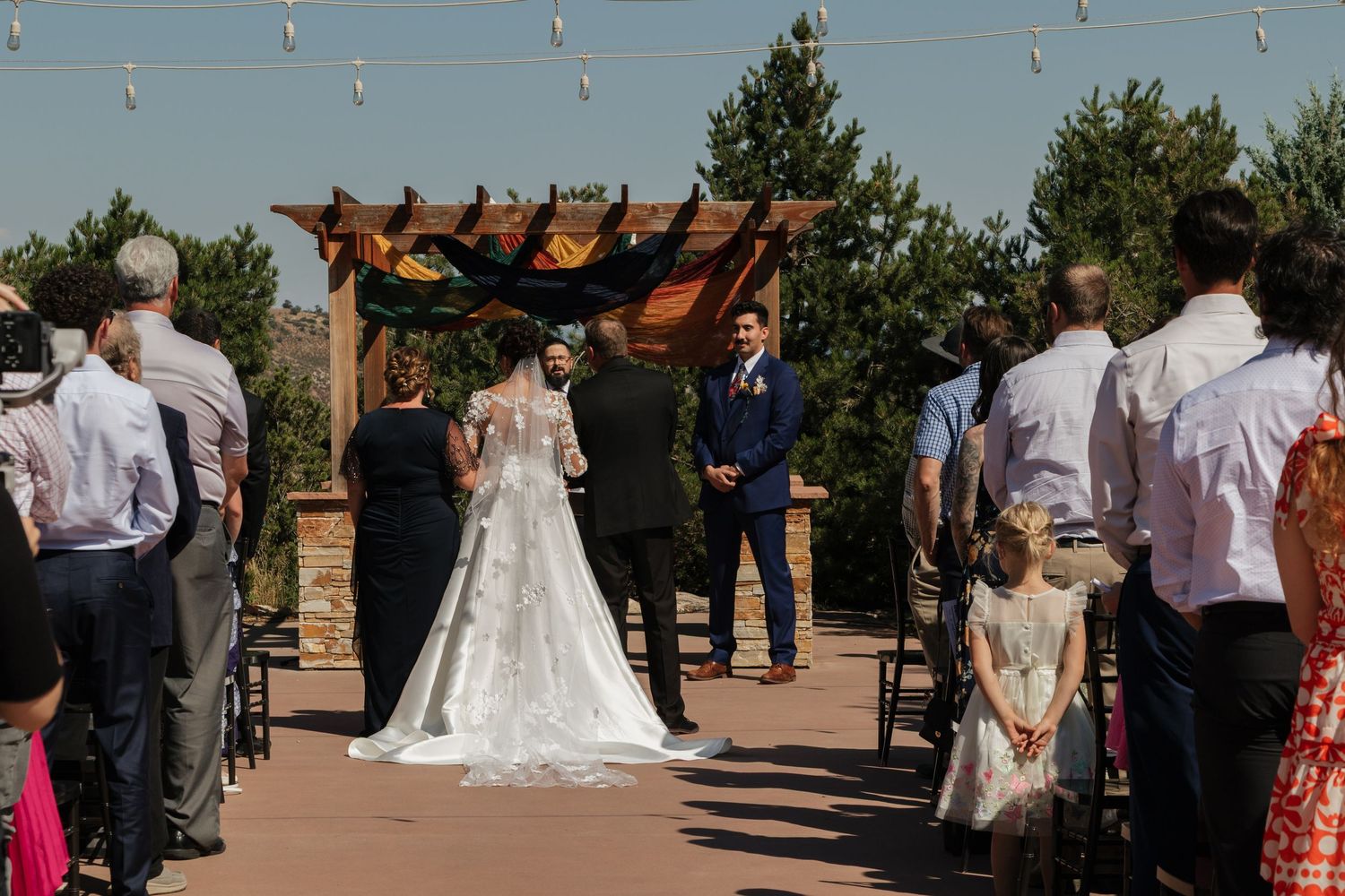 Outdoor wedding ceremony with string lights and mountain scenery in the background.