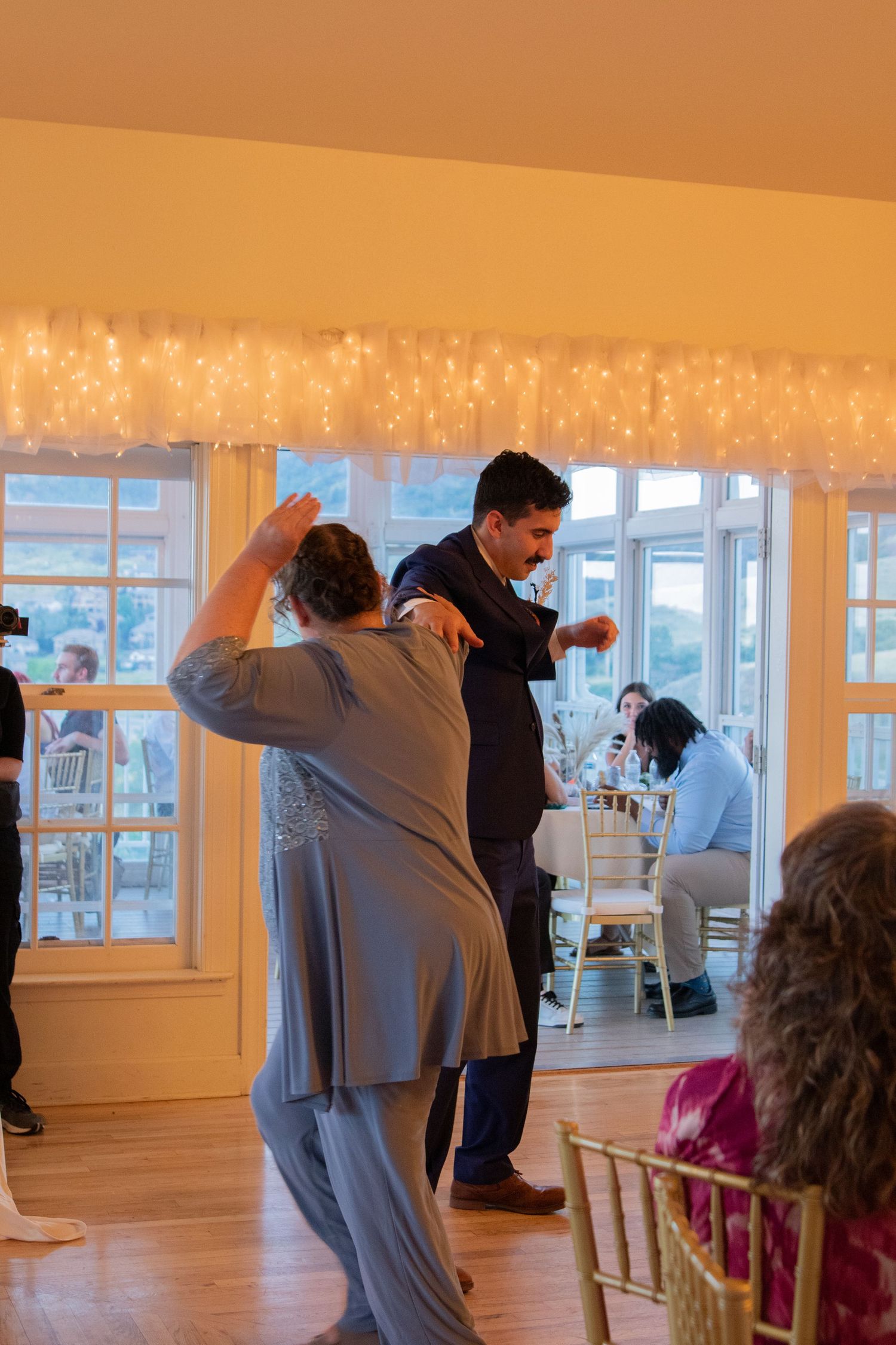 Wedding reception in warm-lit room with string lights and large windows.