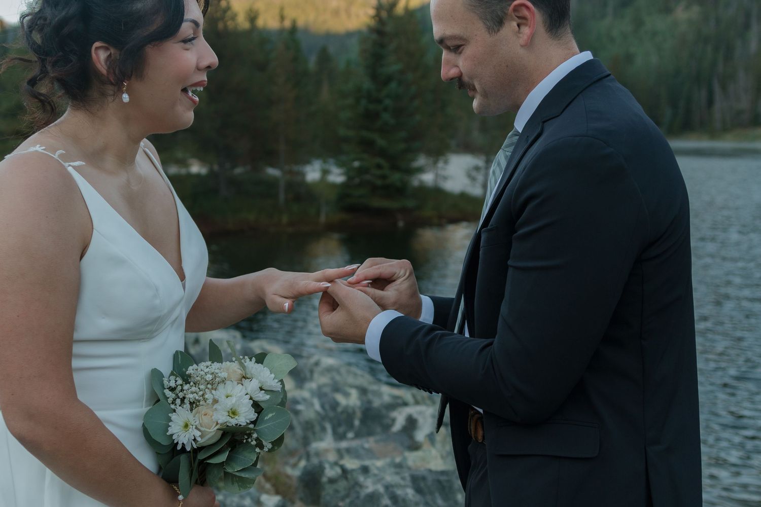 A couple exchanges rings during an intimate lakeside wedding ceremony.