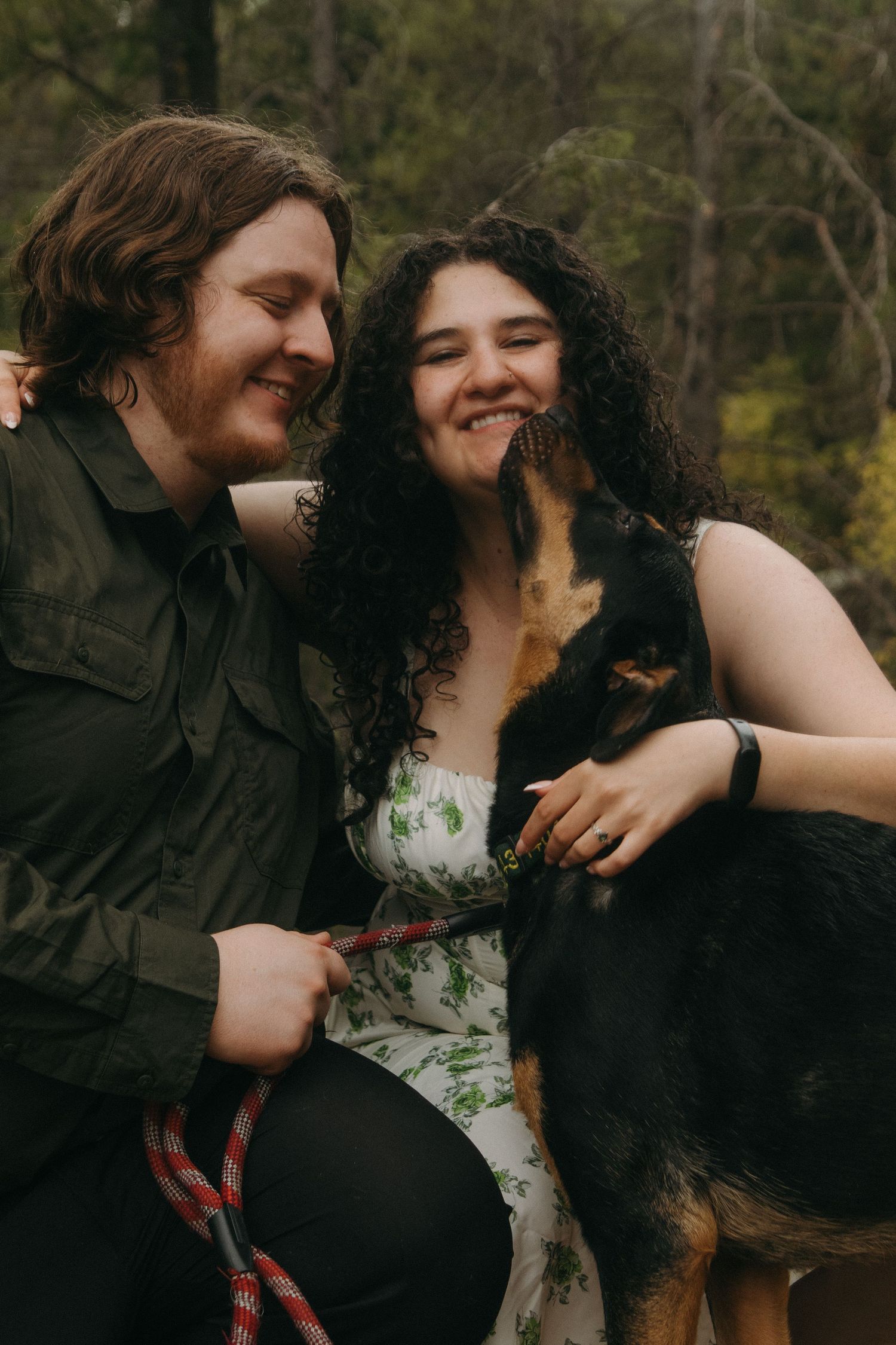 A romantic couple sharing intimate moments outdoors against a natural wooded backdrop.