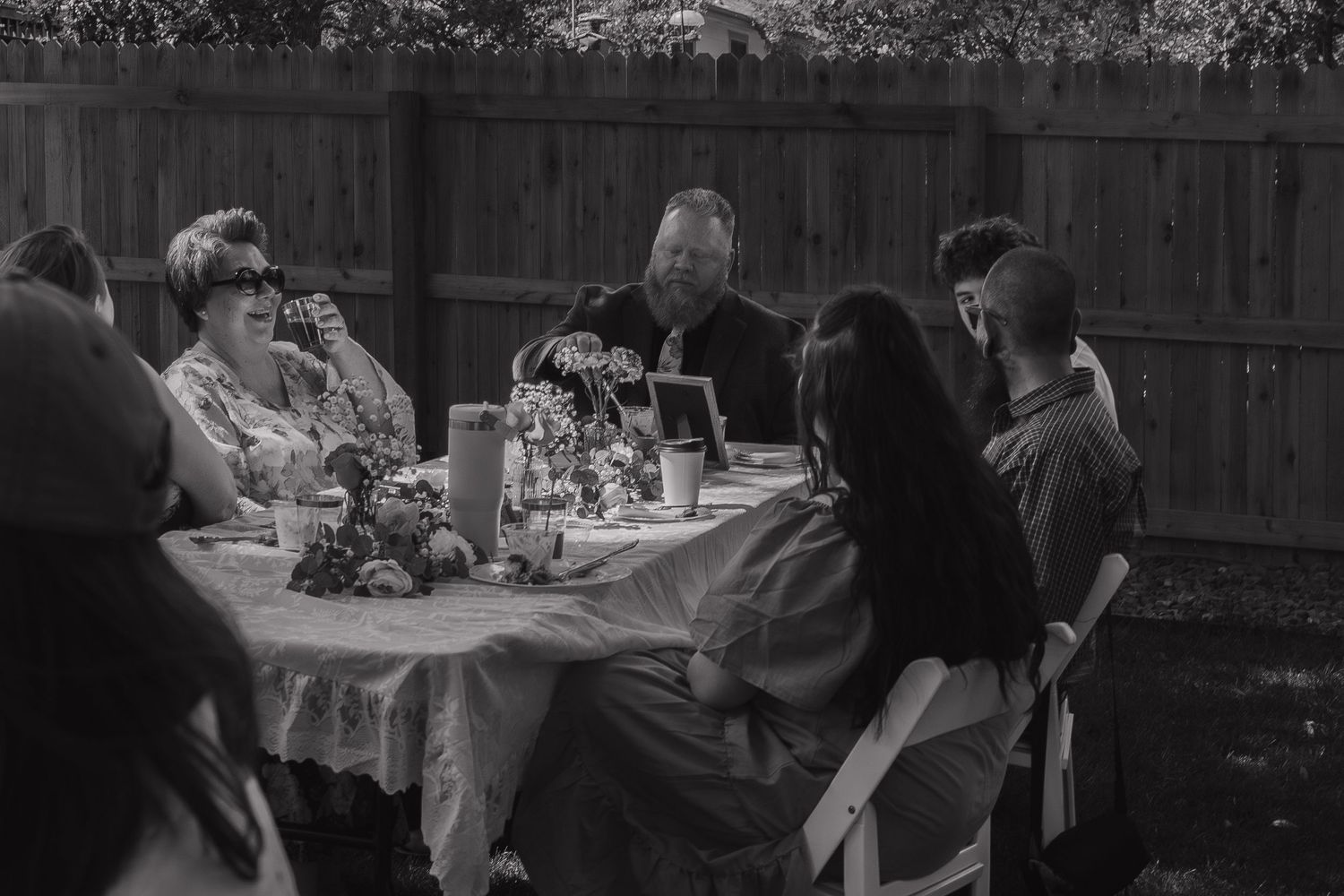 Seven monochrome photographs depict a social gathering or party with people seated at outdoor tables.