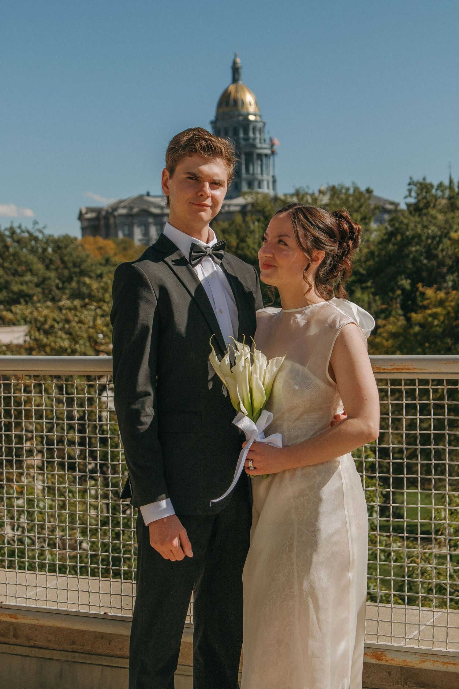 A couple poses for wedding photos on a balcony with a domed building visible in the background.